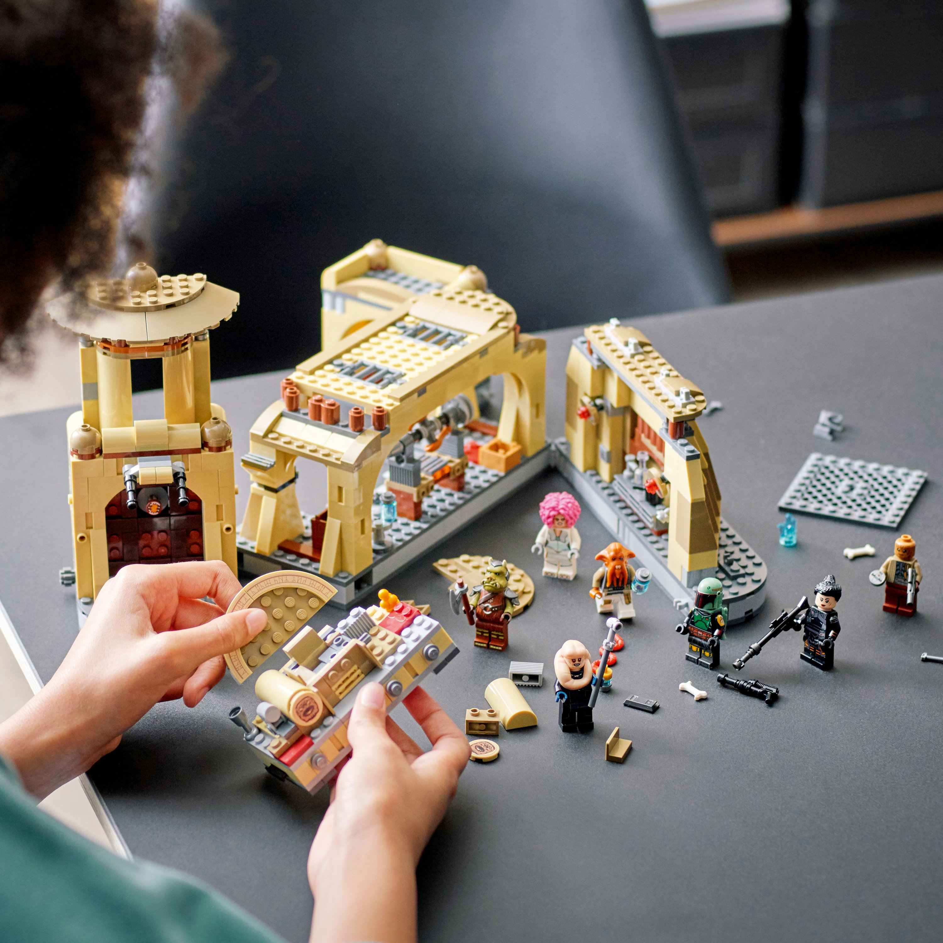 Manos de una persona construyendo un set de Lego Star Wars con figuras y estructuras en una mesa.
