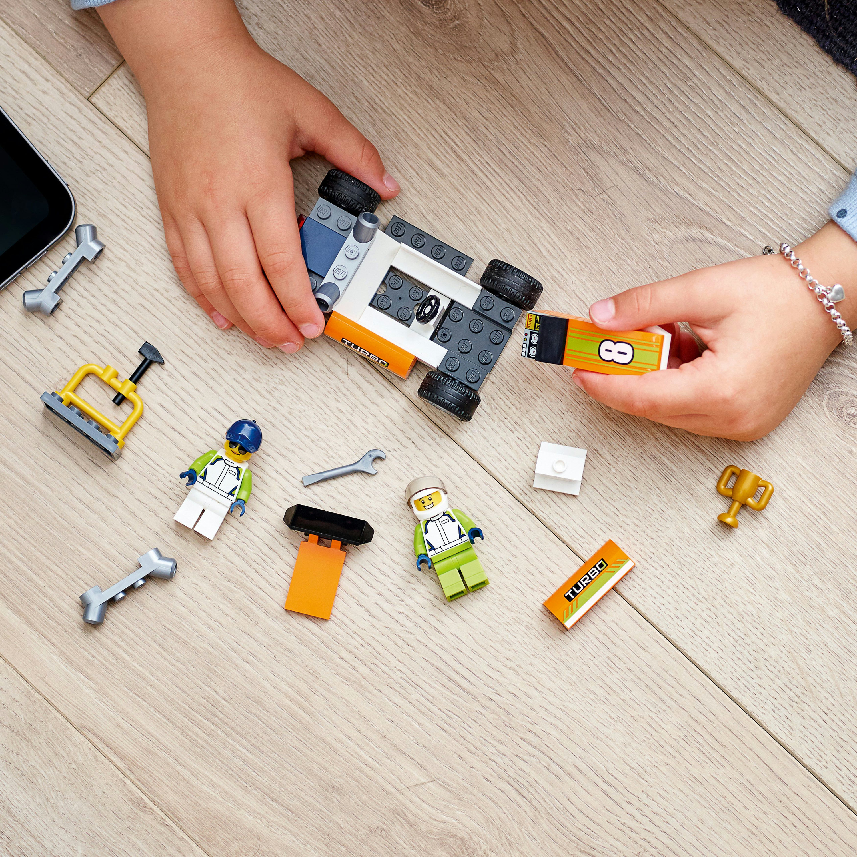 Een kind dat een Lego-automodel in elkaar zet, met onderdelen en figuren verspreid op een houten oppervlak.