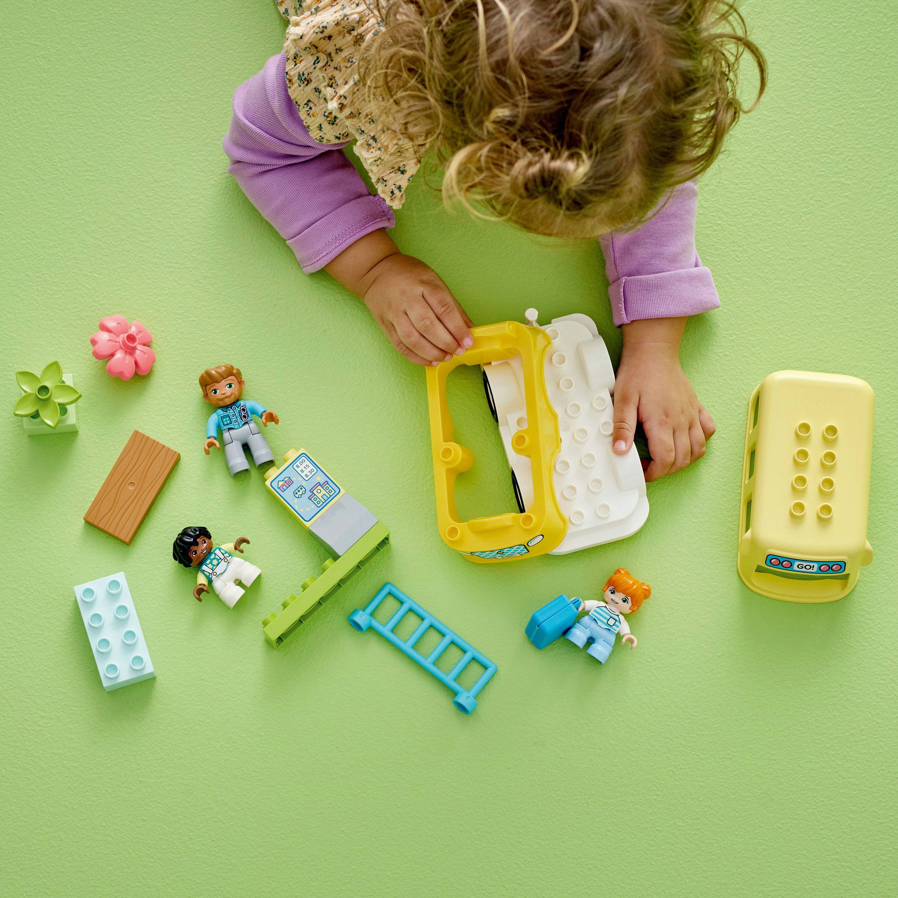 Çocuk Lego Duplo setiyle oynuyor, çeşitli bloklar, figürler ve aksesuarlar yeşil zeminde.