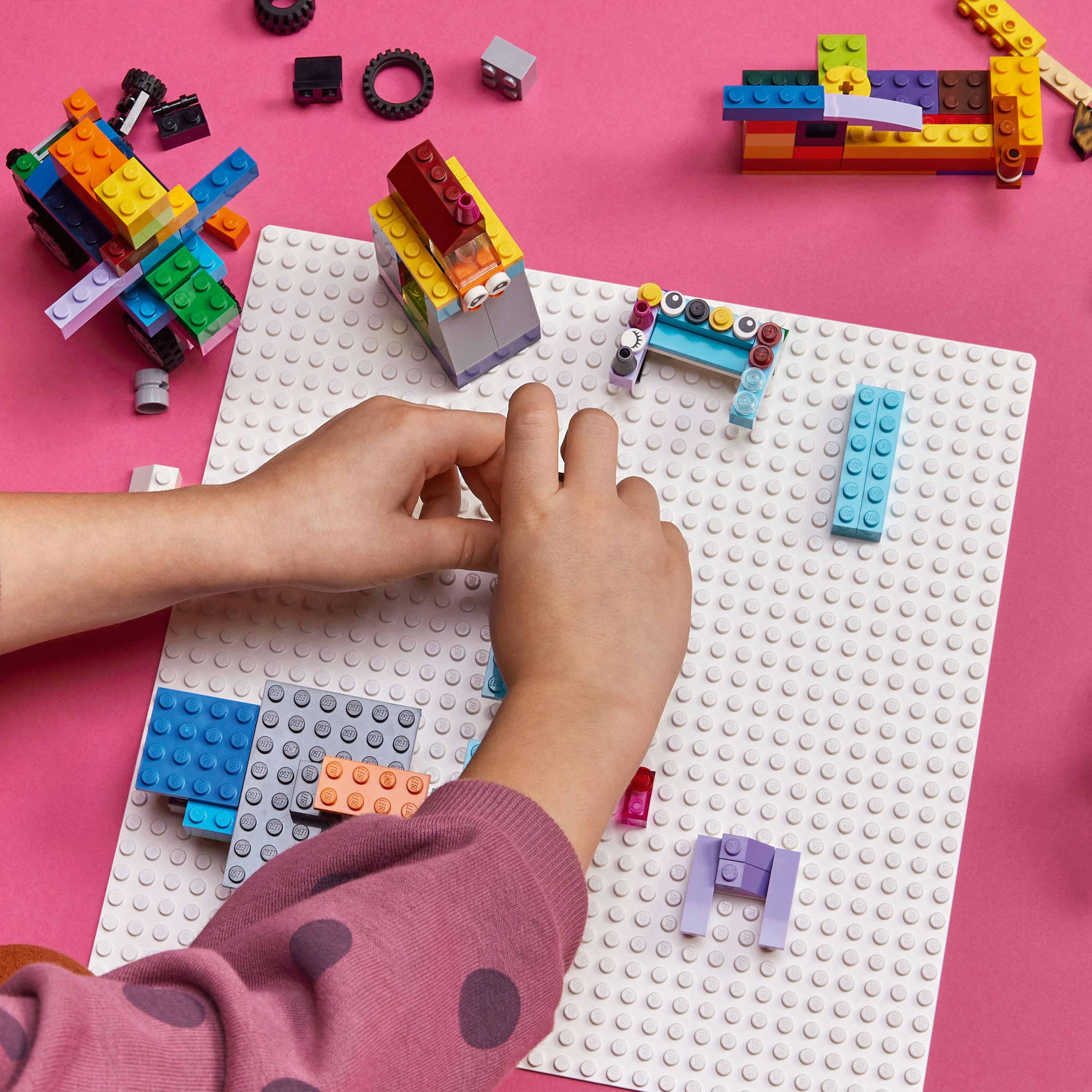 Eller pembe bir yüzeyde Lego blokları ile inşa ediyor. Çeşitli renkli Lego tuğlaları ve bir taban plakası.