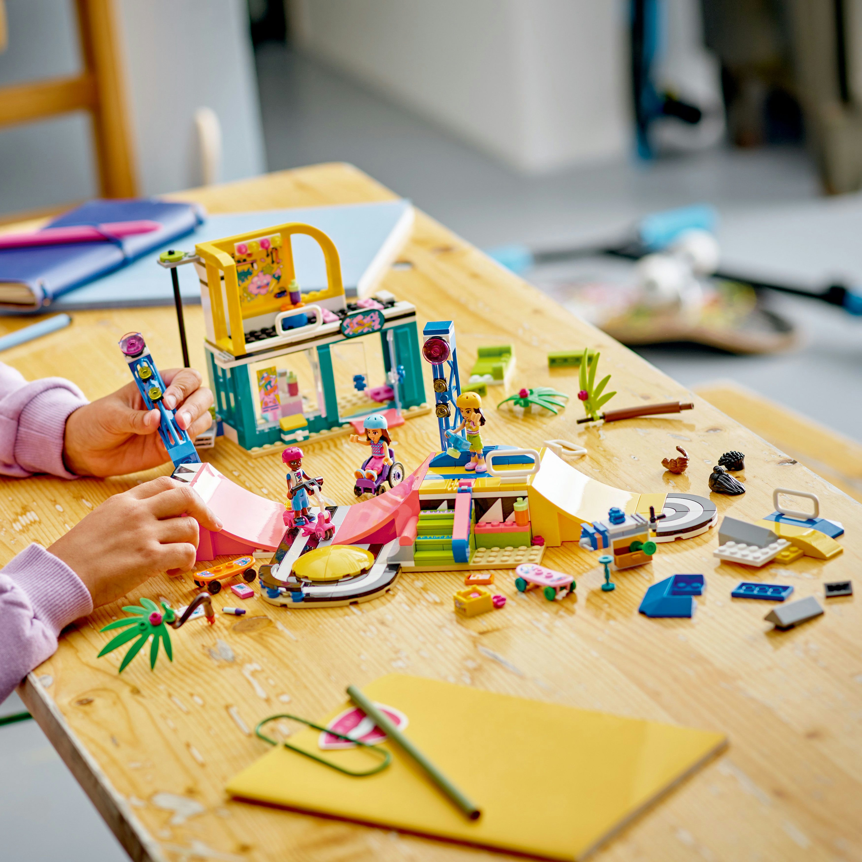 Lego Friends set van een skatepark met figuren, hellingen en accessoires op een houten tafel.