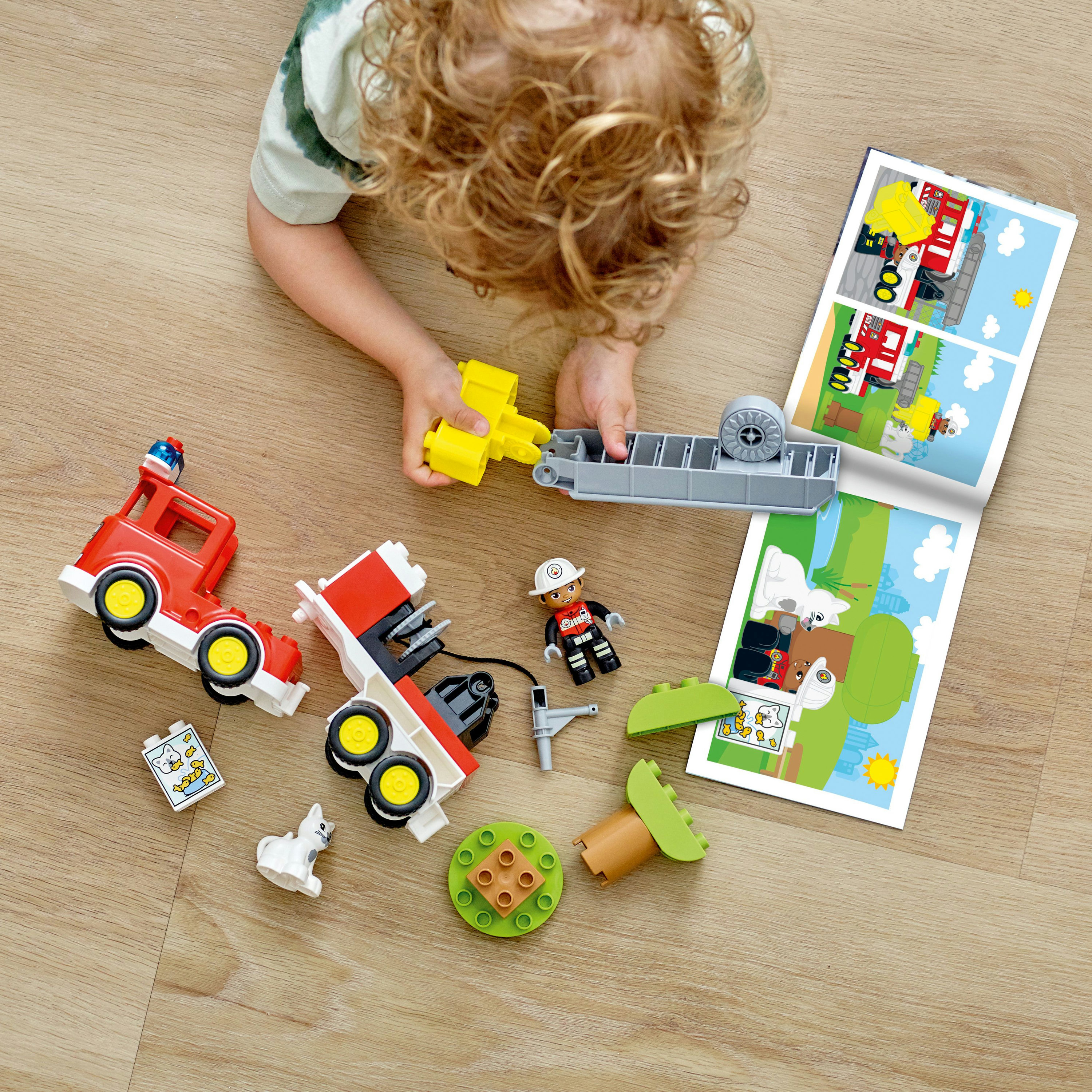 Kind speelt met Duplo brandweerwagen en accessoires. Verspreid op houten vloer.
