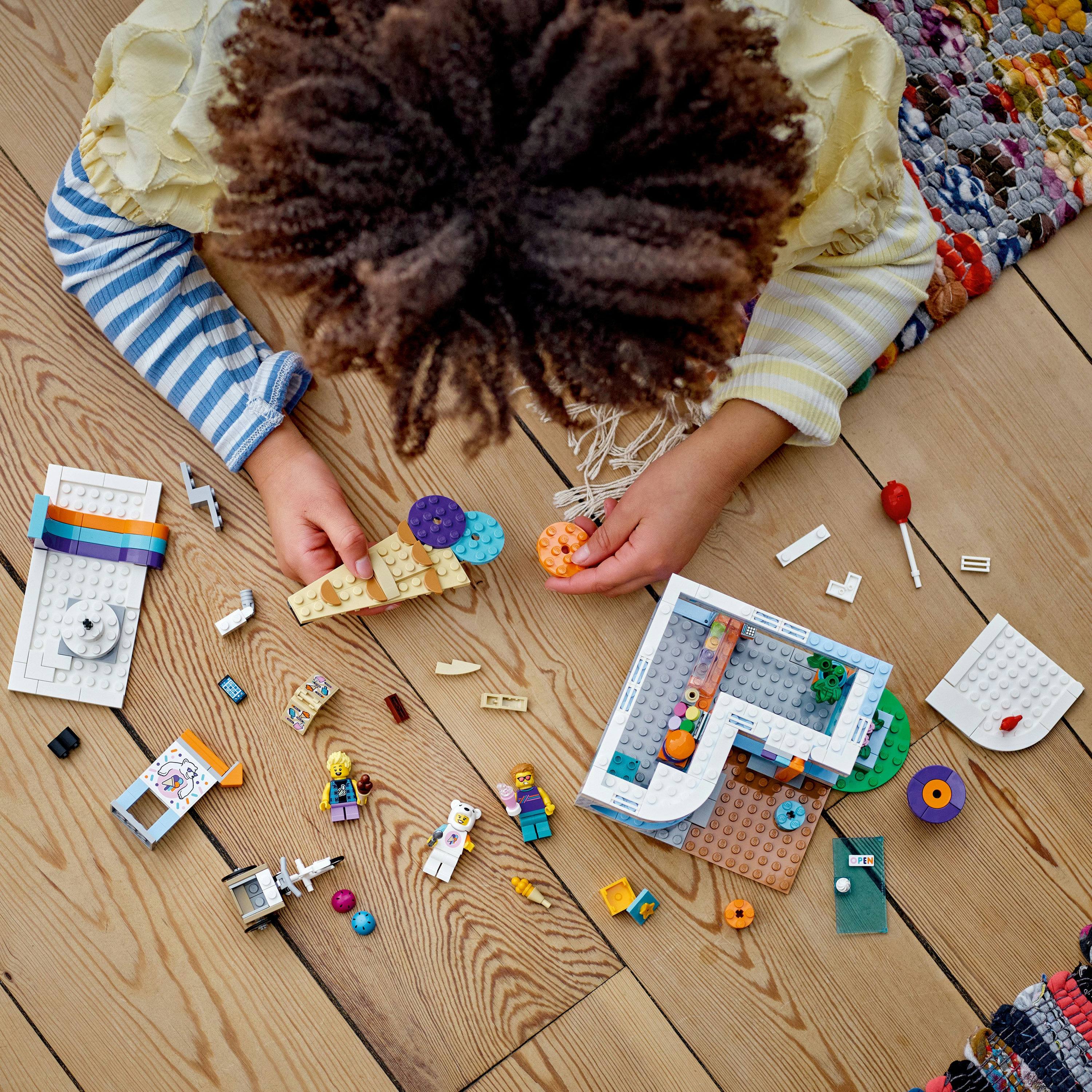 Un bambino che gioca con i mattoncini Lego Friends su un pavimento in legno, con vari modelli.