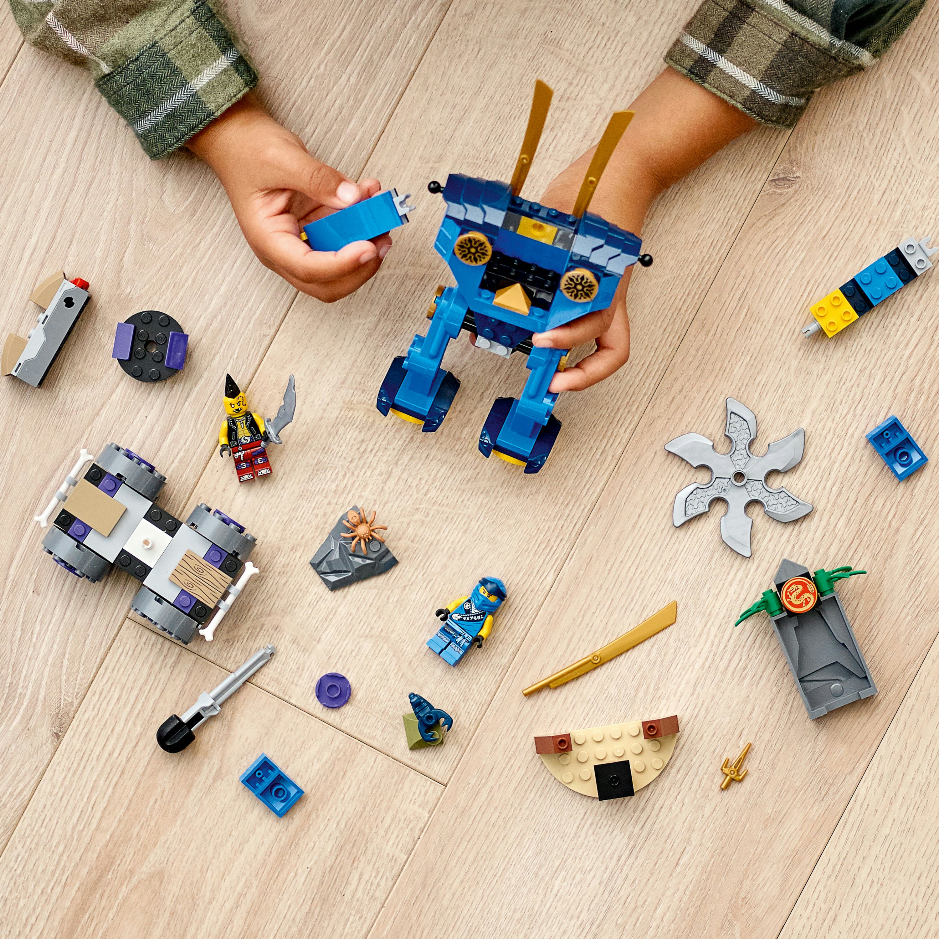 Kinderhände spielen mit Lego Ninjago Teilen. Die Teile sind auf einem Holzboden verteilt.