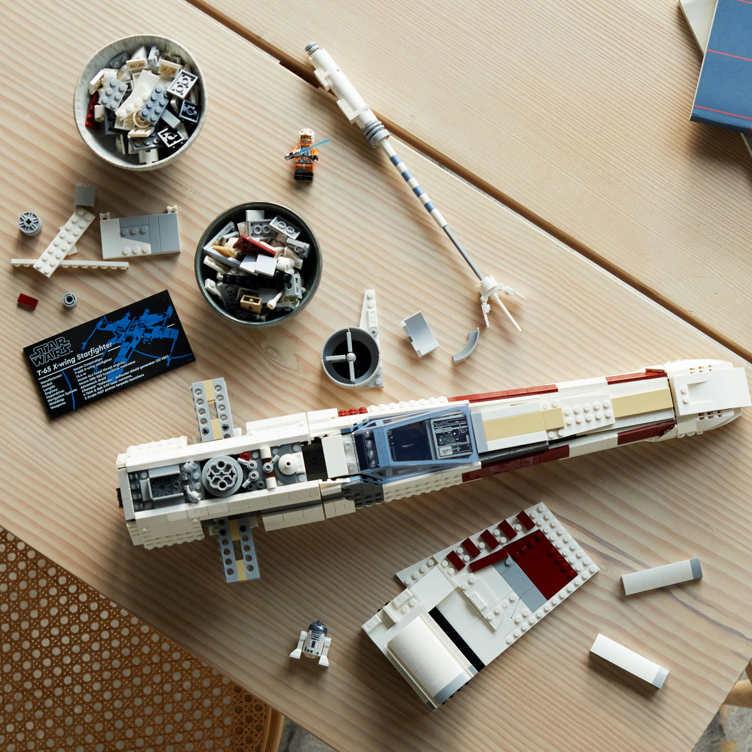 Zestaw Lego X-wing Starfighter, z różnymi elementami, instrukcją i minifigurką na stole.