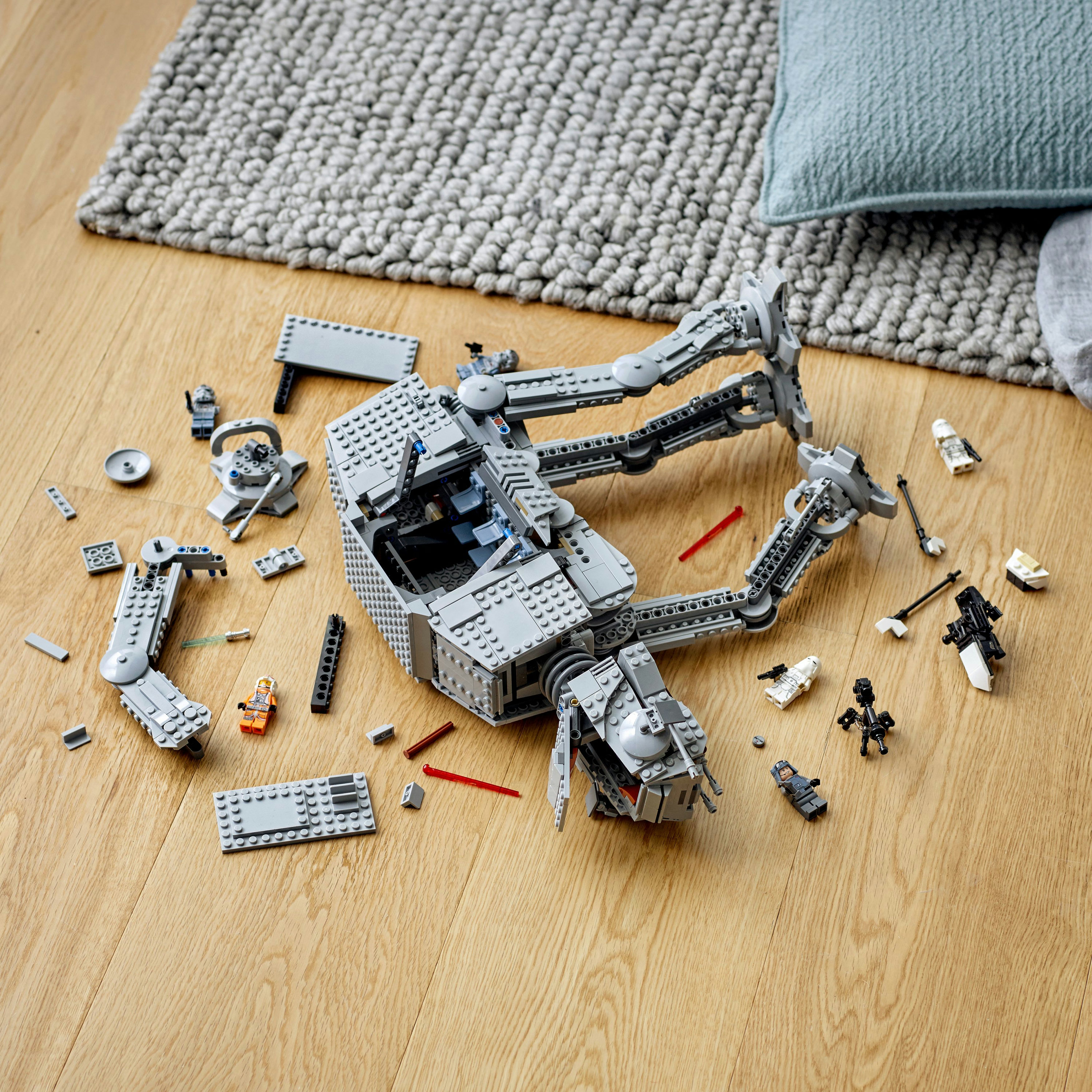 Zdemontowany model LEGO AT-AT na drewnianej podłodze. Rozrzucone części, małe figurki LEGO.