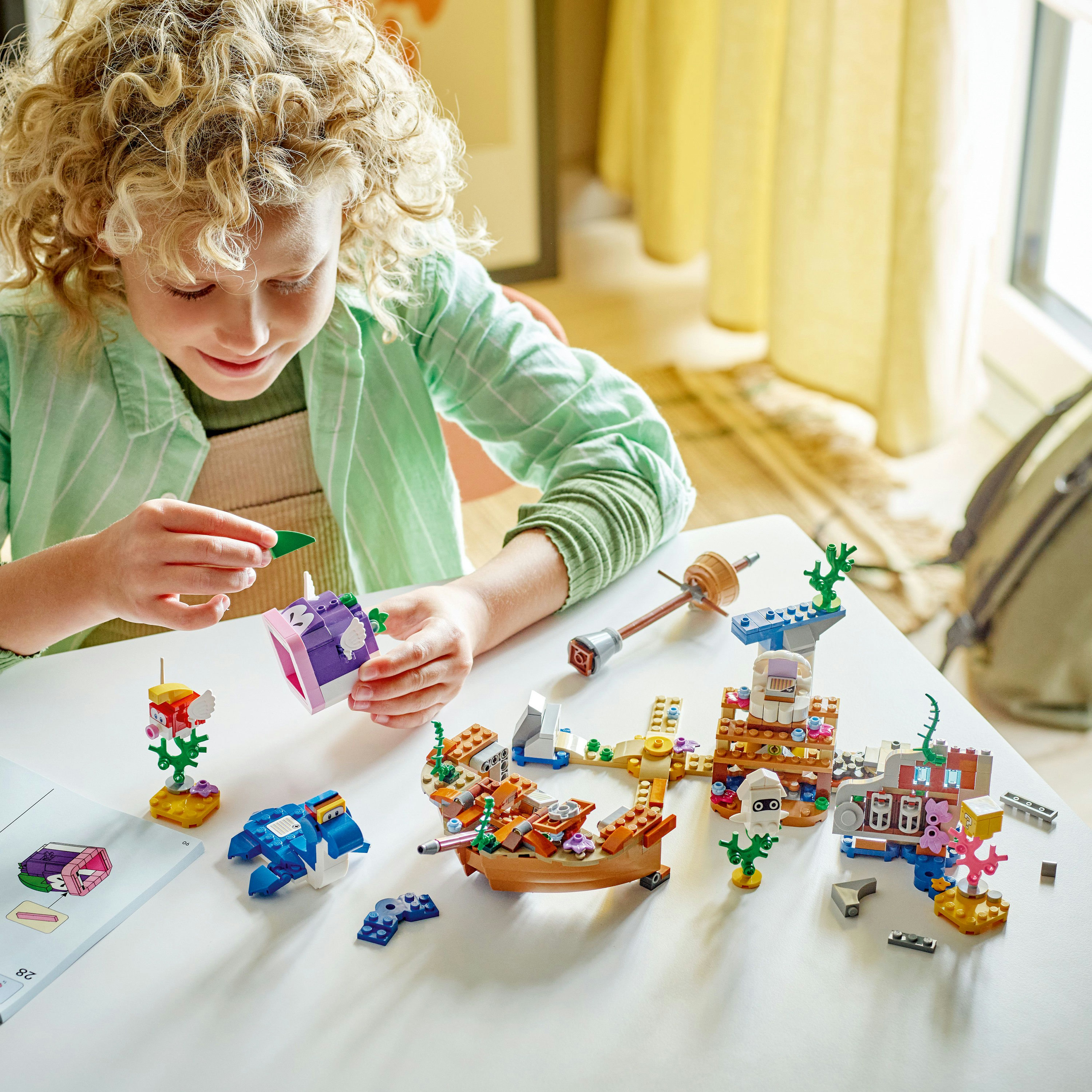 Ein Kind spielt mit einem Lego-Set. Auf einem weißen Tisch befinden sich verschiedene Lego-Konstruktionen und Figuren.