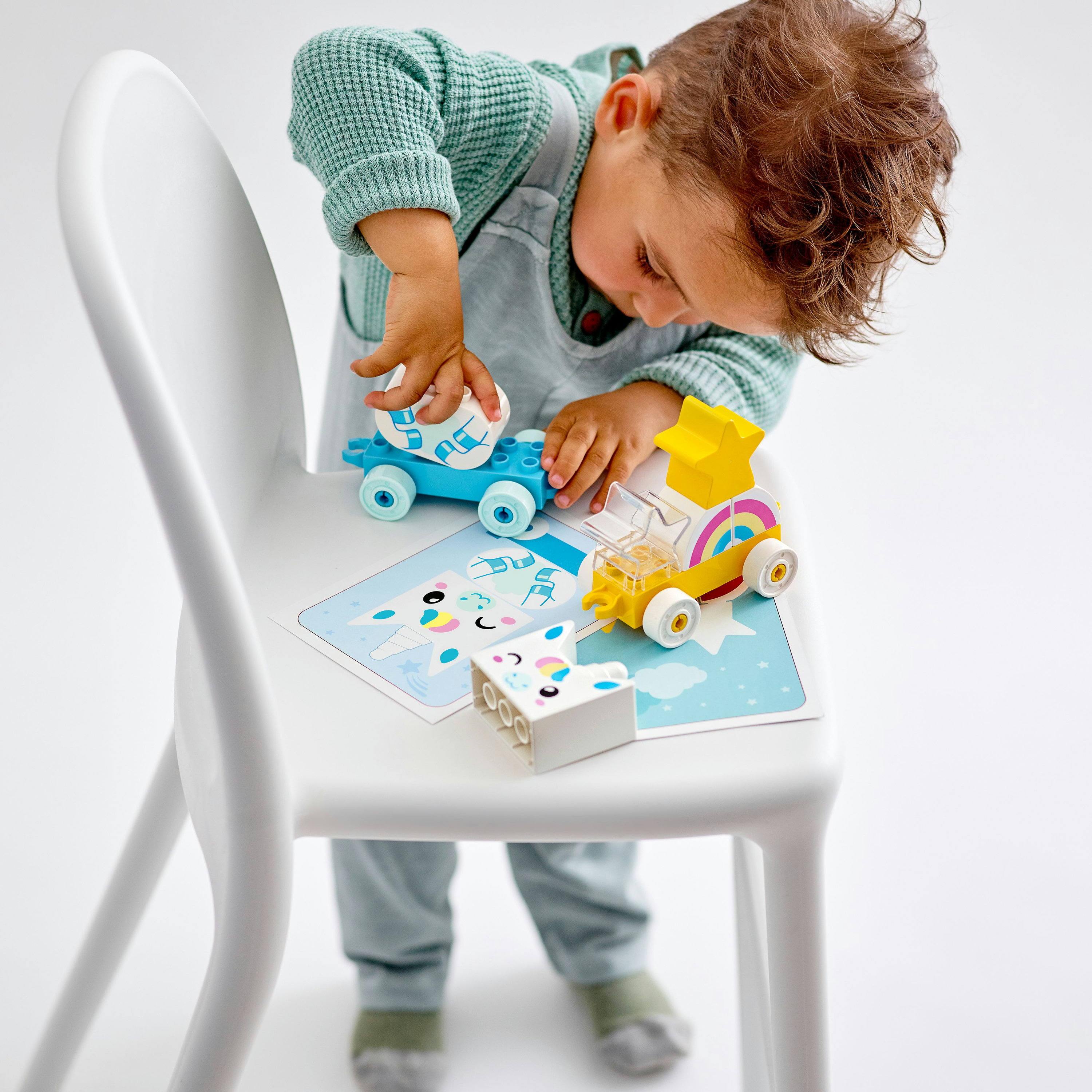Ein Kind spielt mit Lego Duplo Autos. Eines ist blau, das andere gelb, beide auf einer Spielmatte.