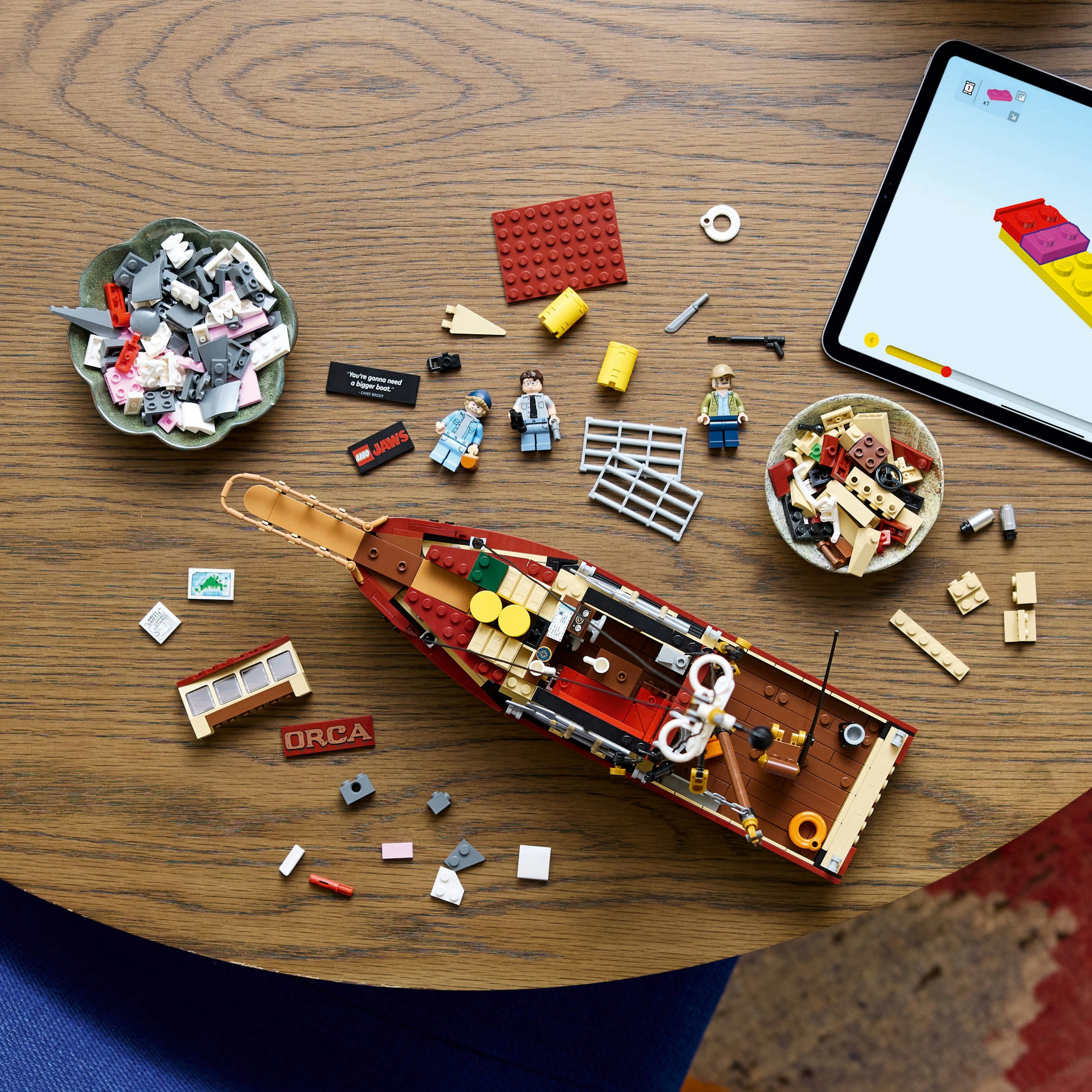 Model łodzi Lego z różnymi częściami i figurkami na drewnianym stole.