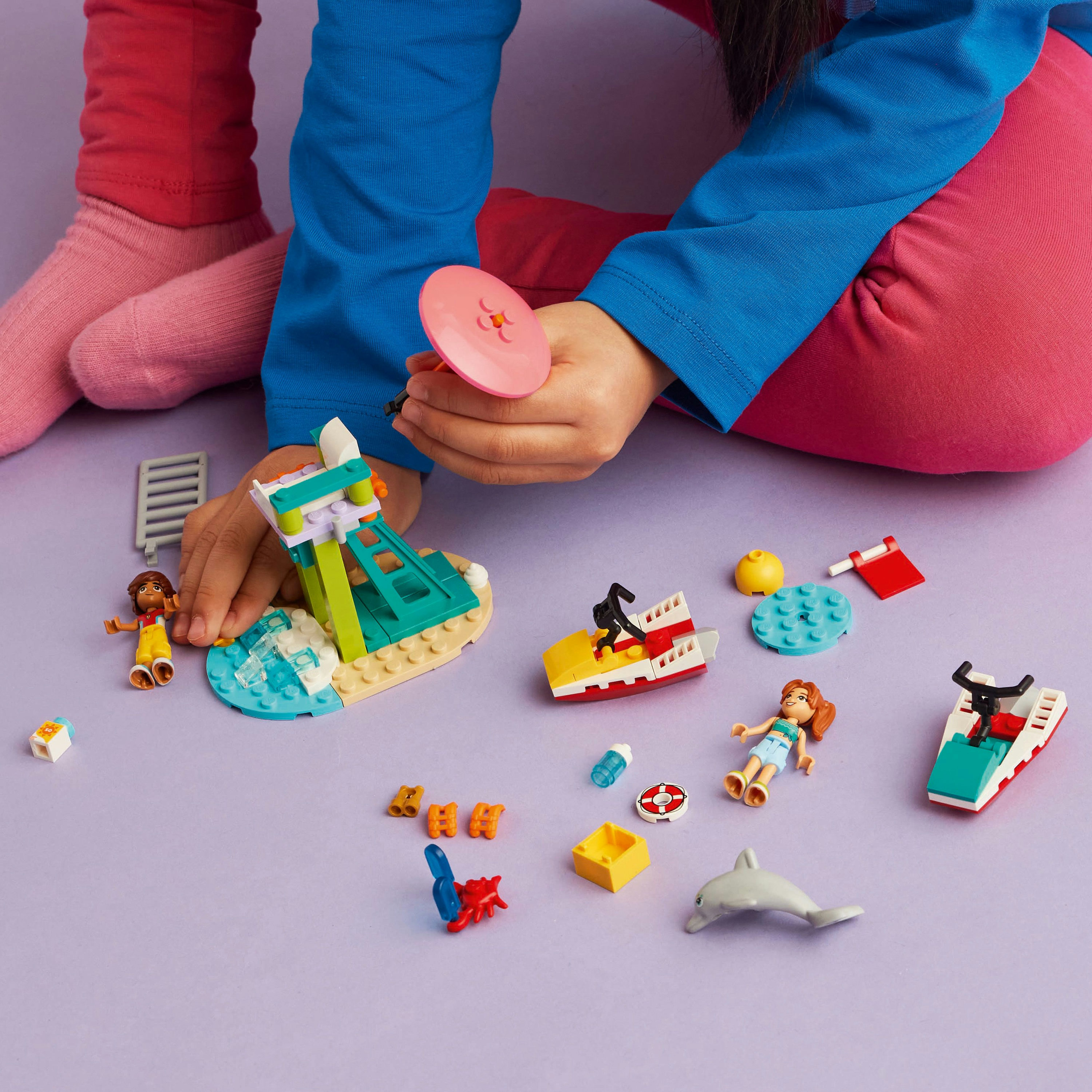 Dziecko bawi się zestawem Lego Friends. Zawiera scenę na plaży, figurki i małe łodzie.