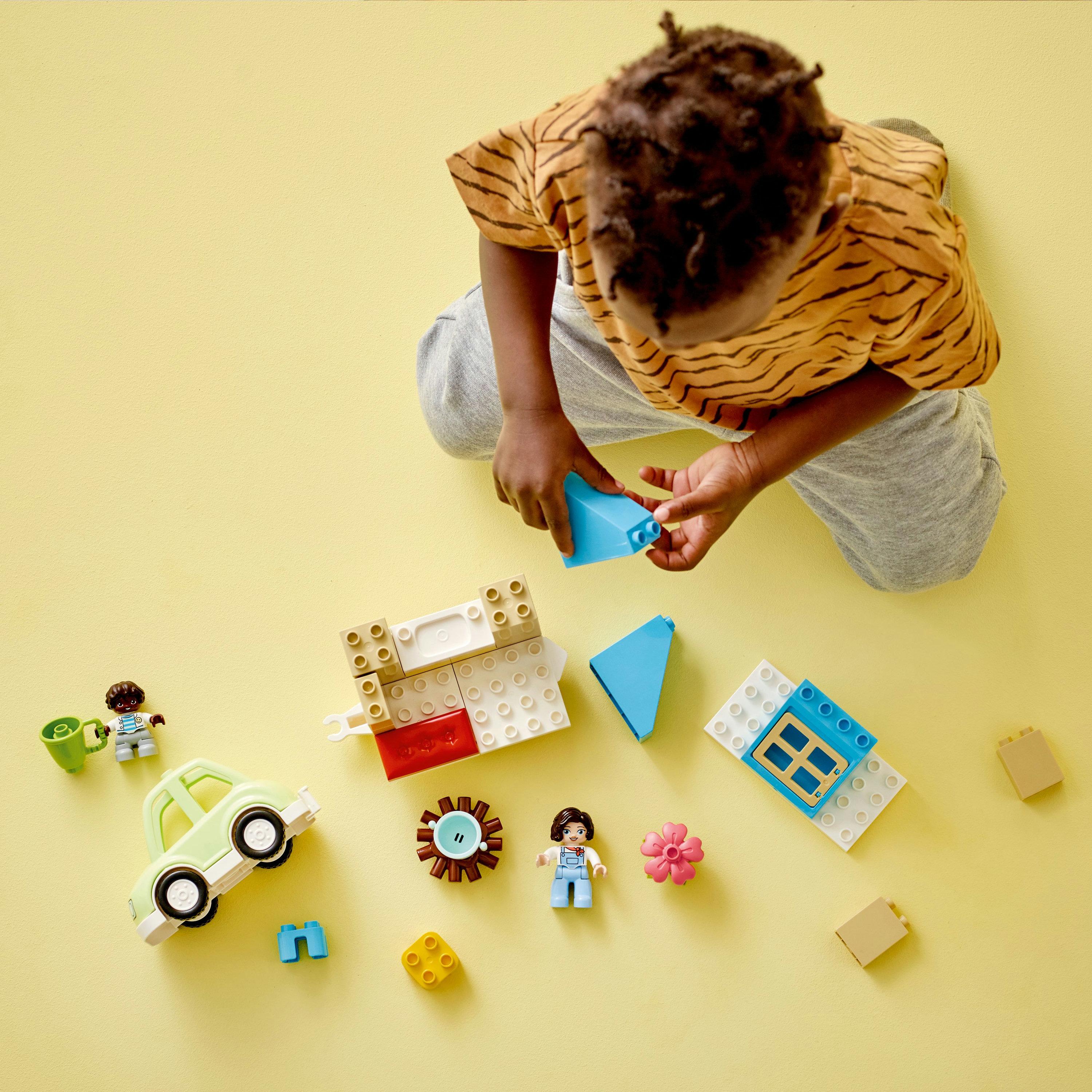 Ein Kind spielt mit LEGO Duplo-Blöcken, baut mit einem Auto, einer Blume und Figuren.
