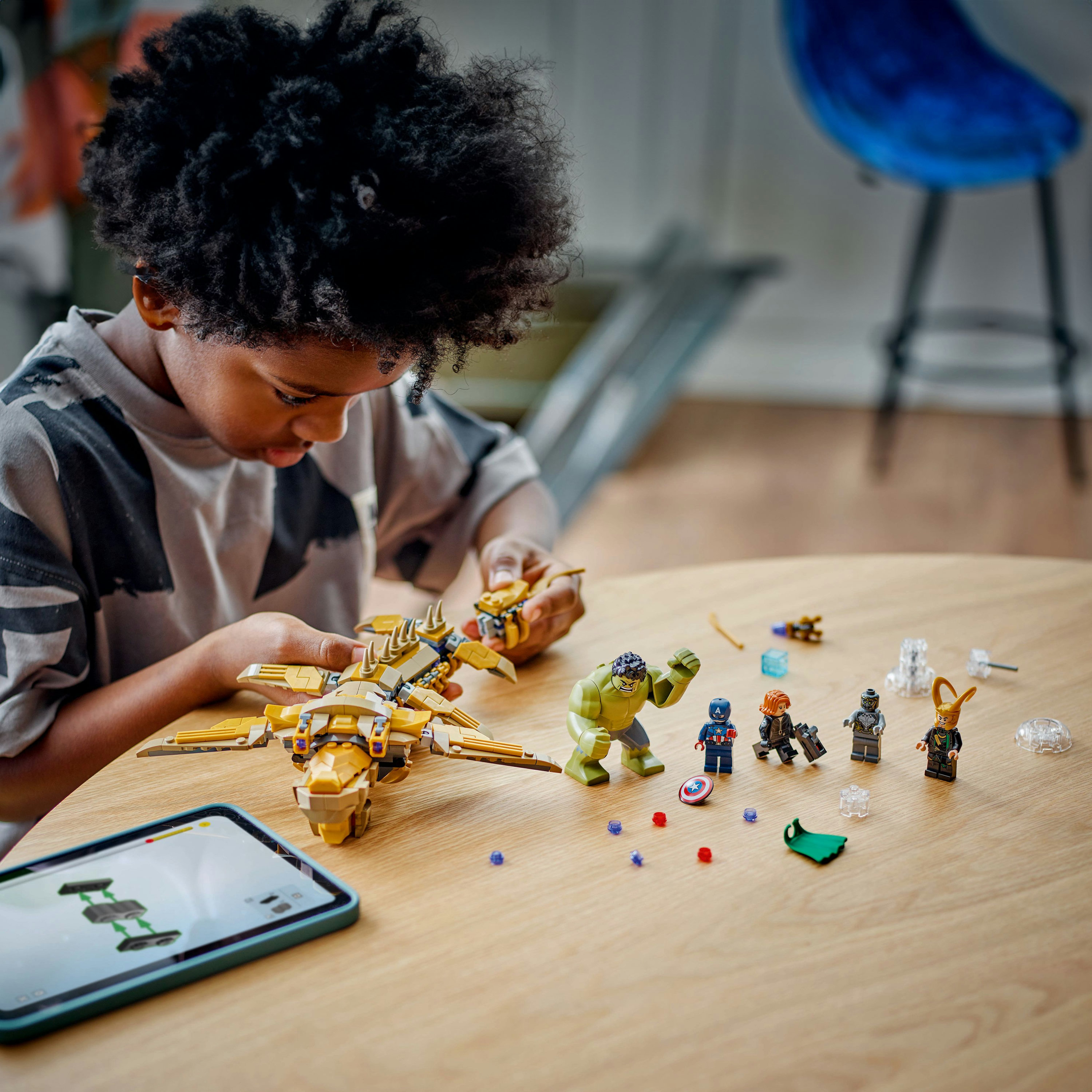 Un bambino assembla un set Lego Marvel con personaggi e un jet, su un tavolo di legno.