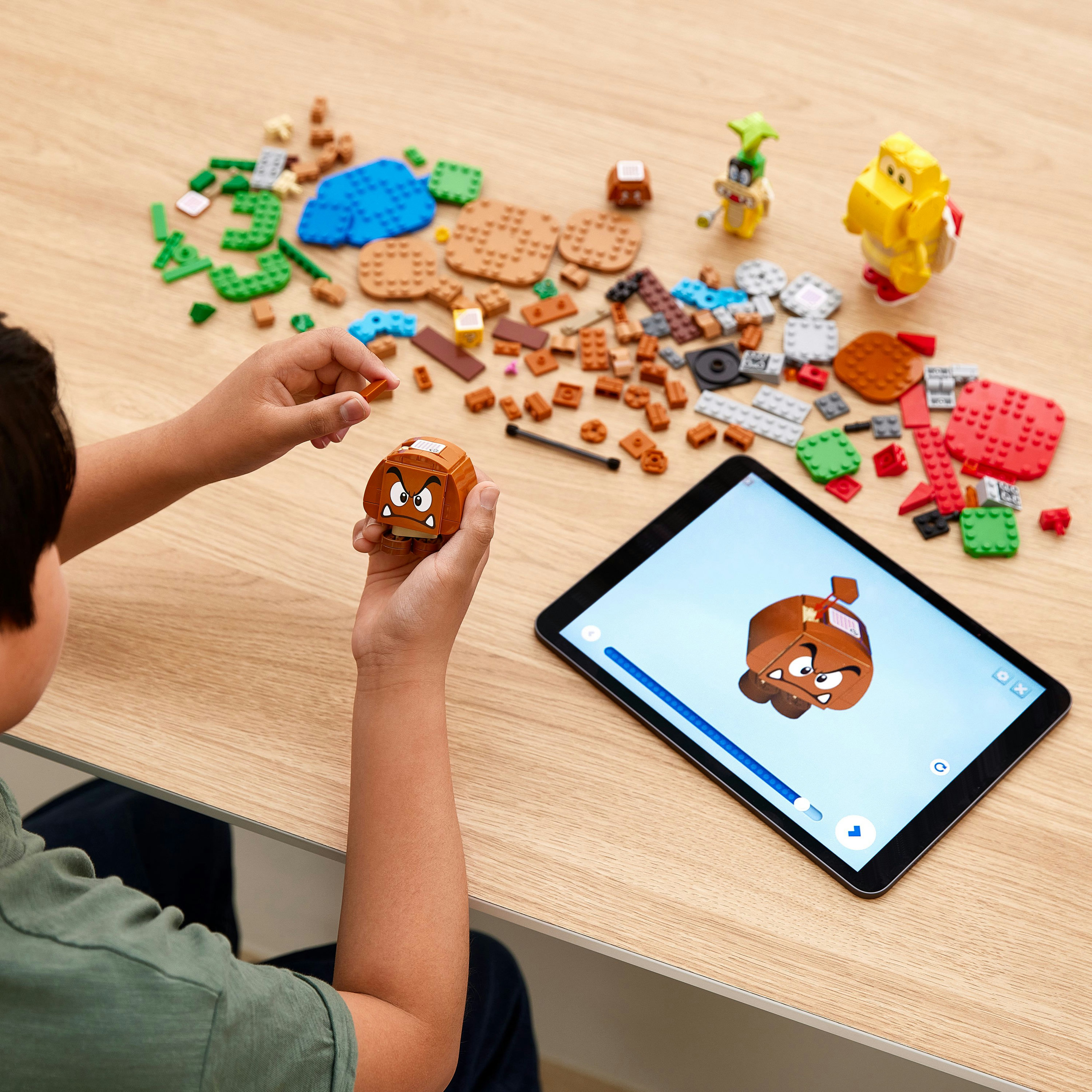 Dziecko trzymające Lego Goomba, oglądające tablet z obrazem Goomba.