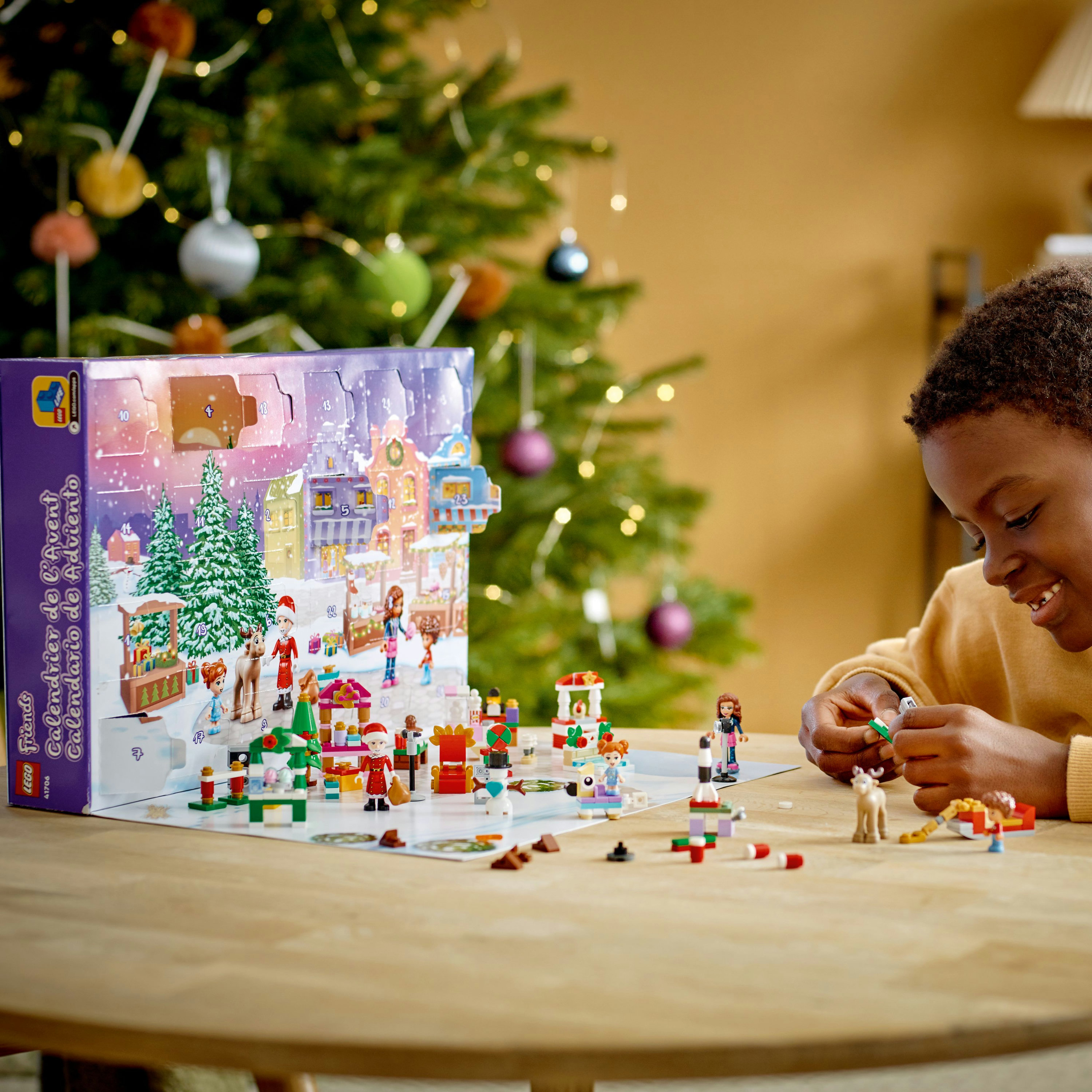 Ein Kind spielt mit einem Lego Friends Adventskalender-Set. Das Set steht auf einem Tisch mit einem Weihnachtsbaum.