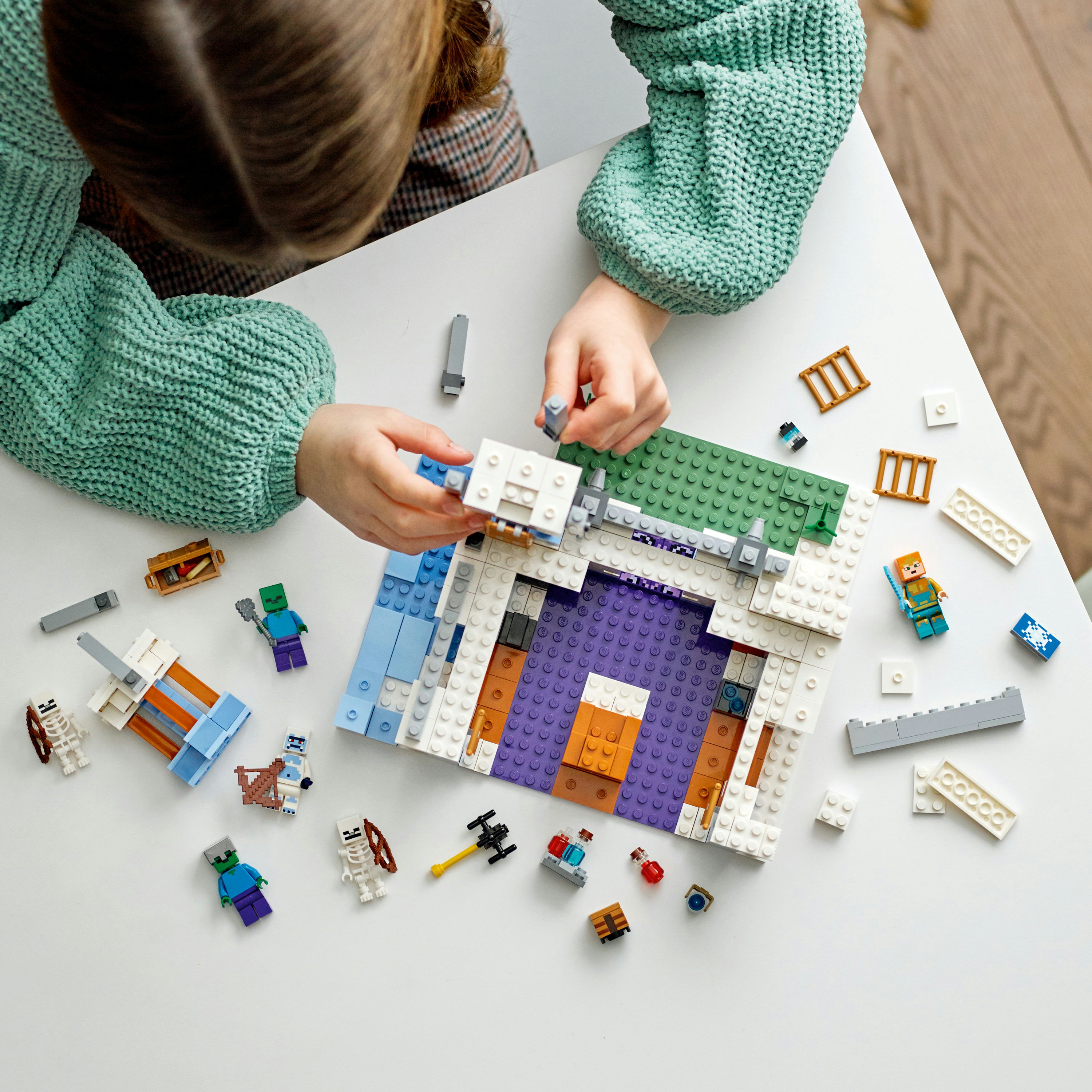Ein Kind, das ein Lego Minecraft-Set zusammenbaut. Enthält Figuren, Blöcke und Zubehör auf einem weißen Tisch.