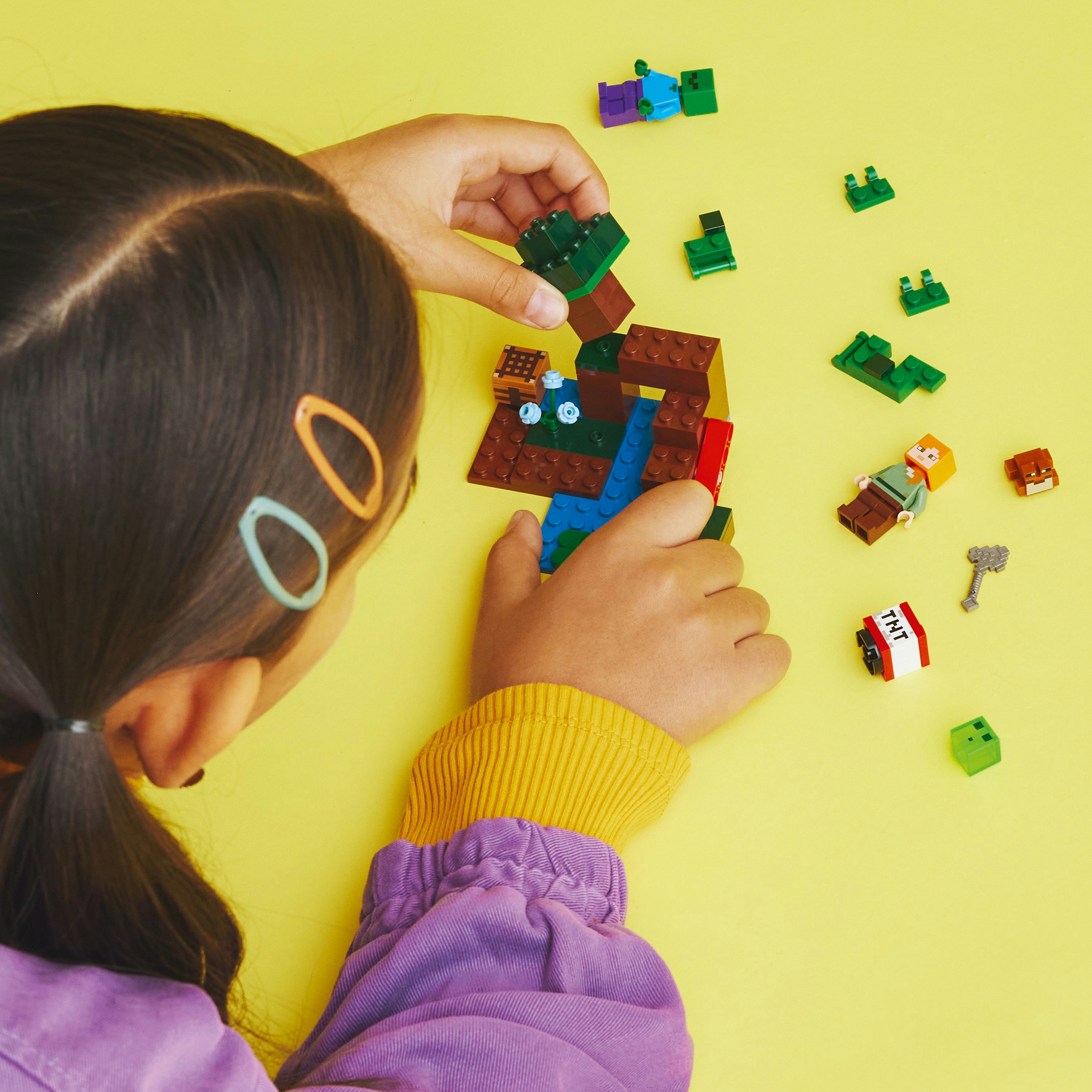 Ein Kind, das mit LEGO-Steinen auf einer gelben Oberfläche baut.