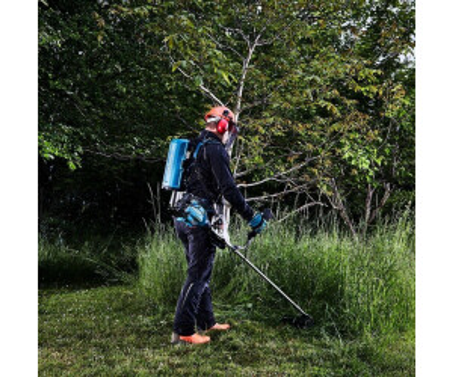 Una persona con equipo de protección utiliza una recortadora de hilo en una zona con hierba cerca de árboles y arbustos.