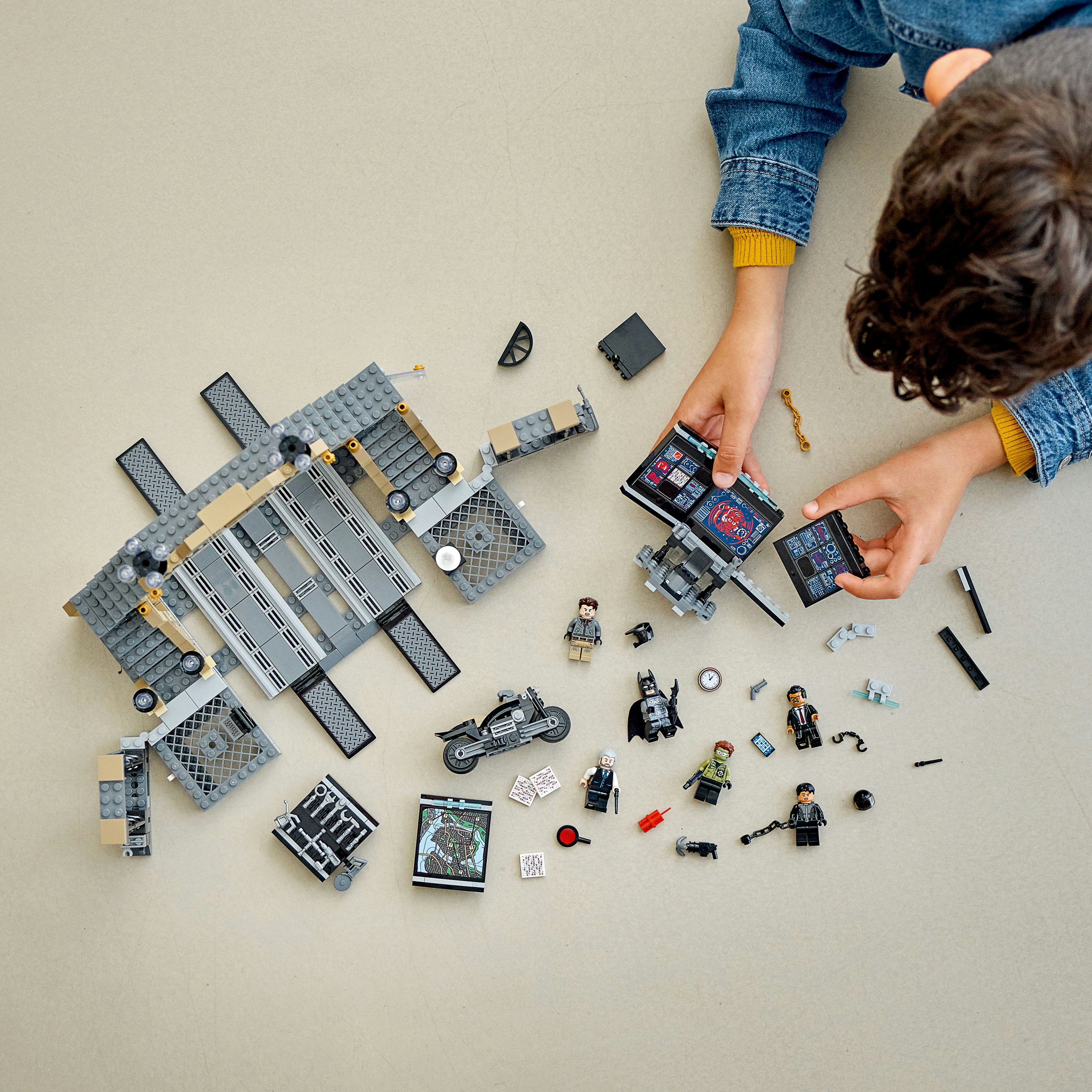 Un bambino sta costruendo un set LEGO sul pavimento. Il set ha molte minifigure e parti di veicoli.