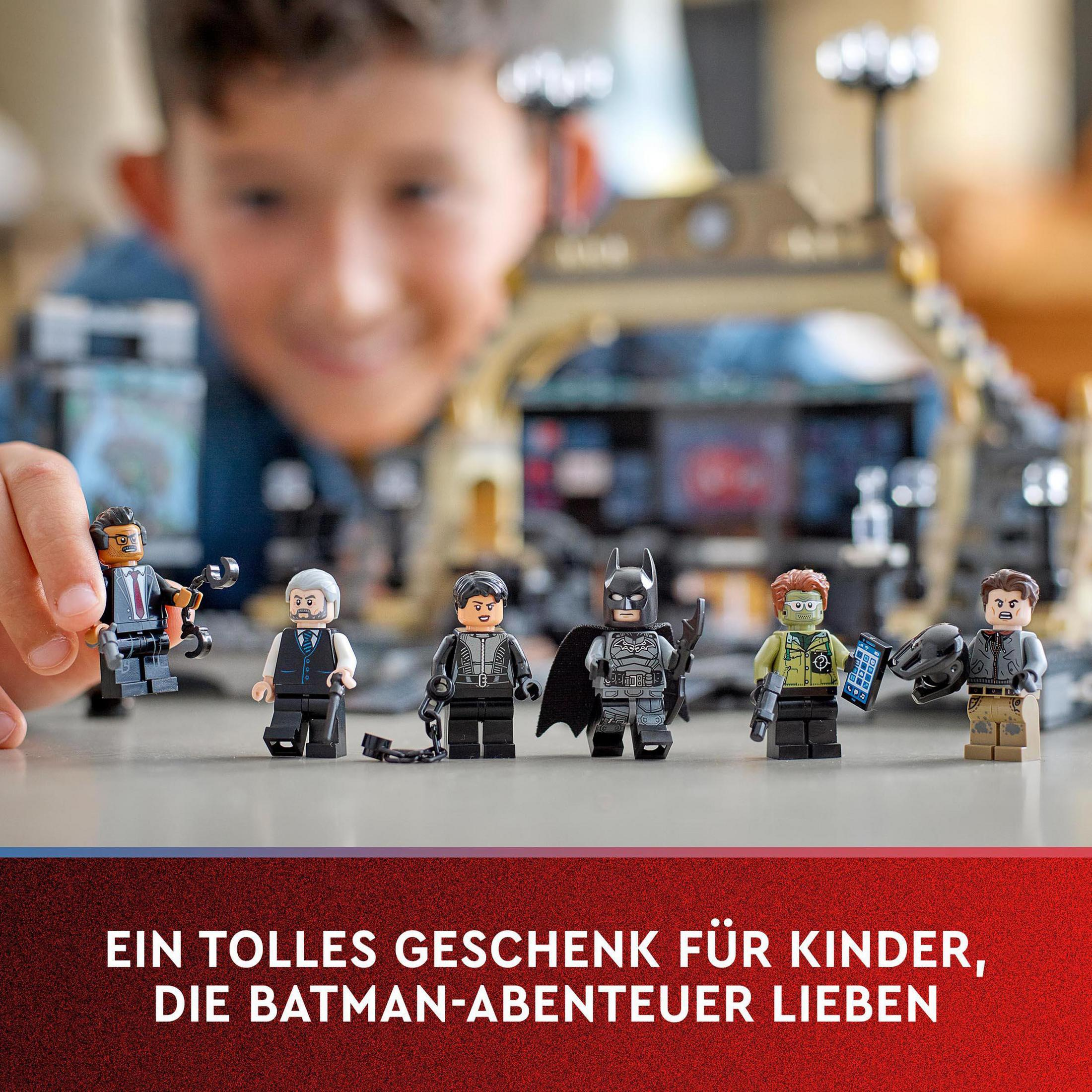 Un ragazzo gioca con i personaggi Lego Batman. I personaggi sono su un tavolo. Lo sfondo è sfocato.