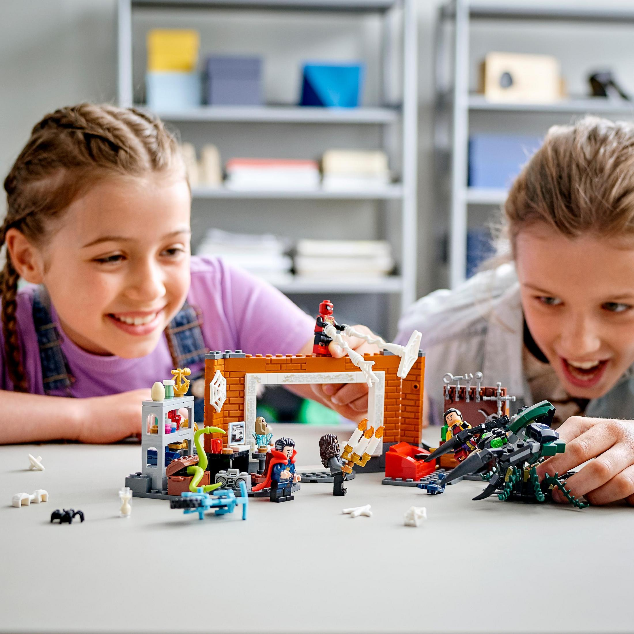 Dwoje uśmiechniętych dzieci bawi się zestawem Lego. Figurki i konstrukcje Lego na białym stole.