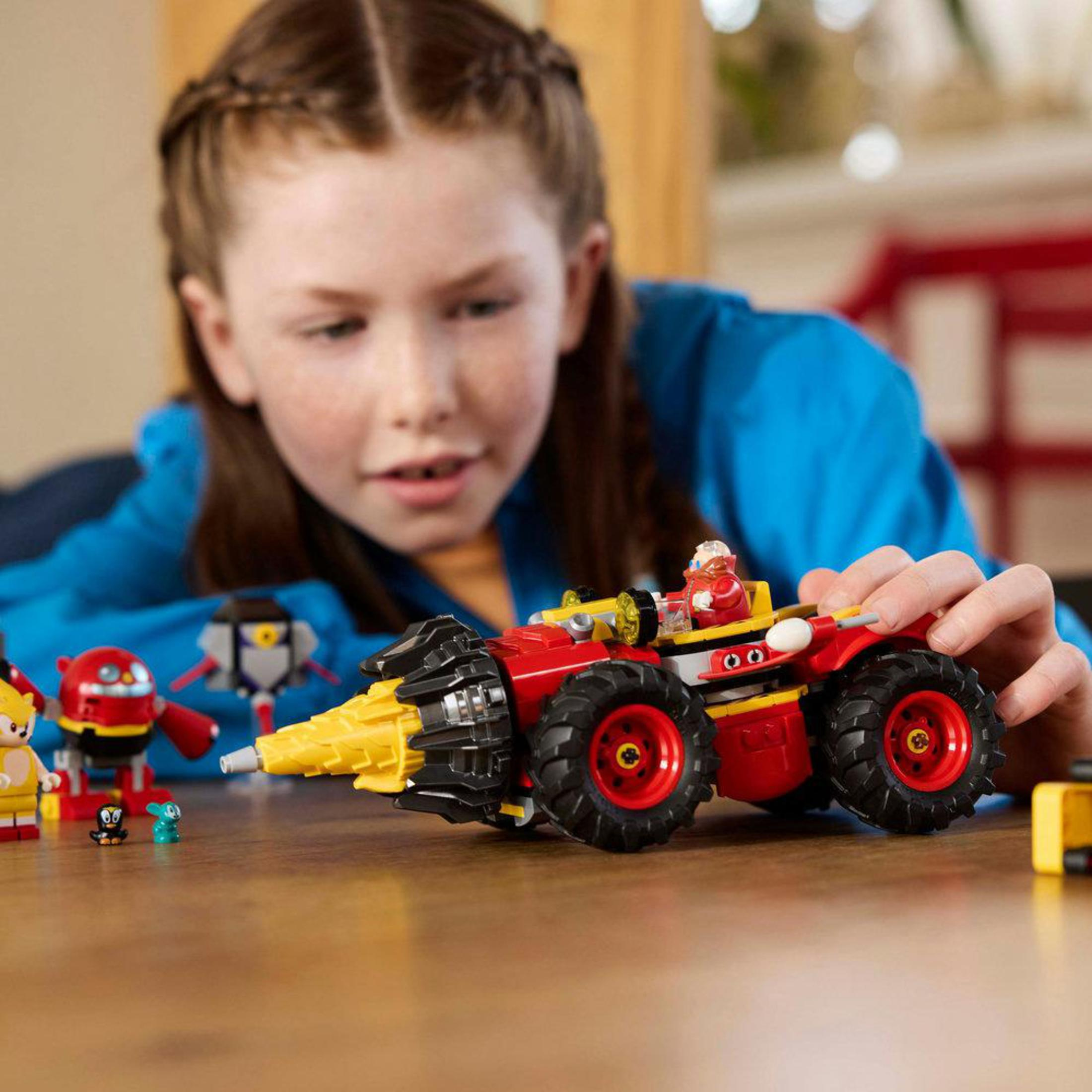 Ein Mädchen spielt mit einem Lego-Auto-Spielzeug mit einem gelben Bohrer in einem Raum.