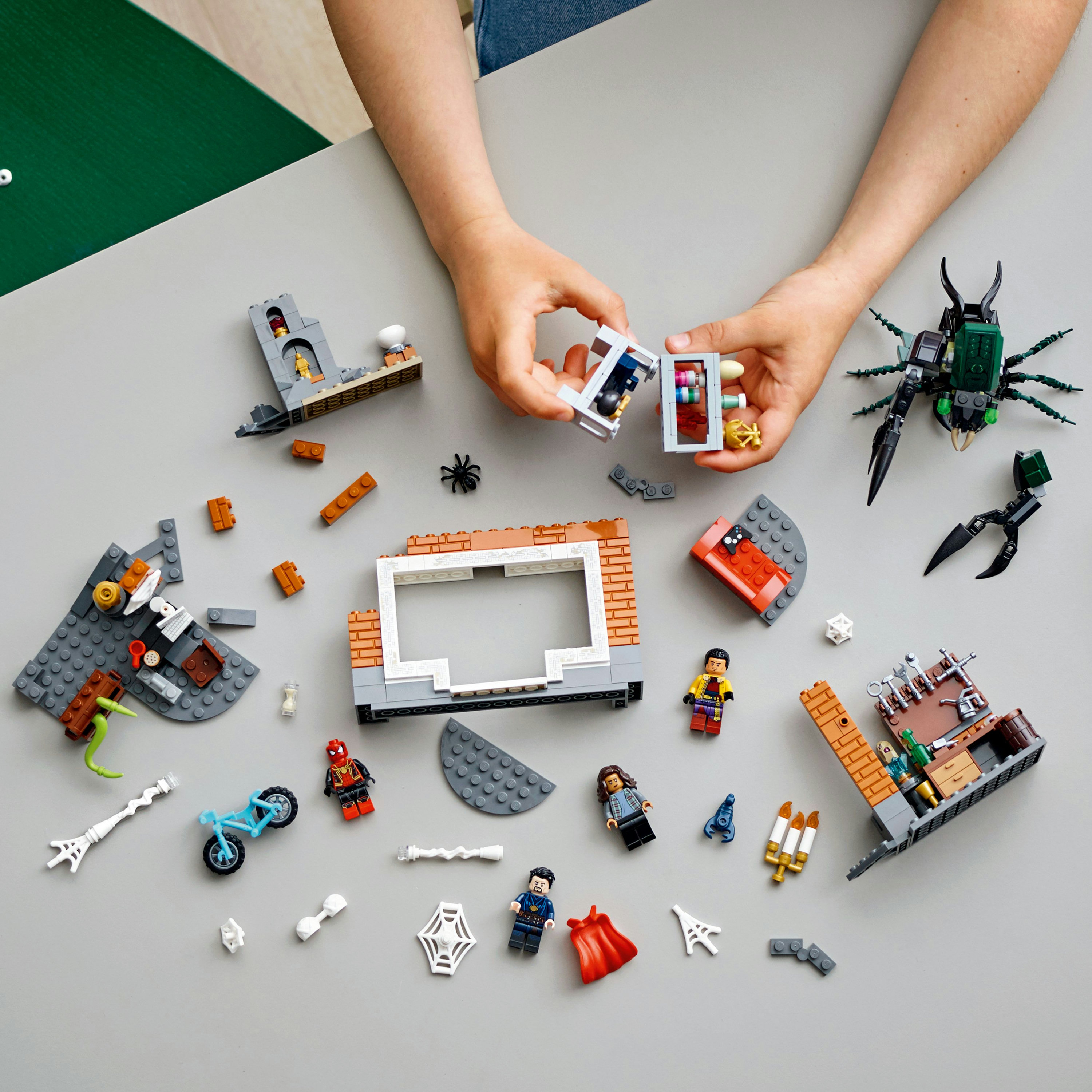 Stół z rozrzuconymi klockami i figurkami Lego, z rękami składającymi scenę.