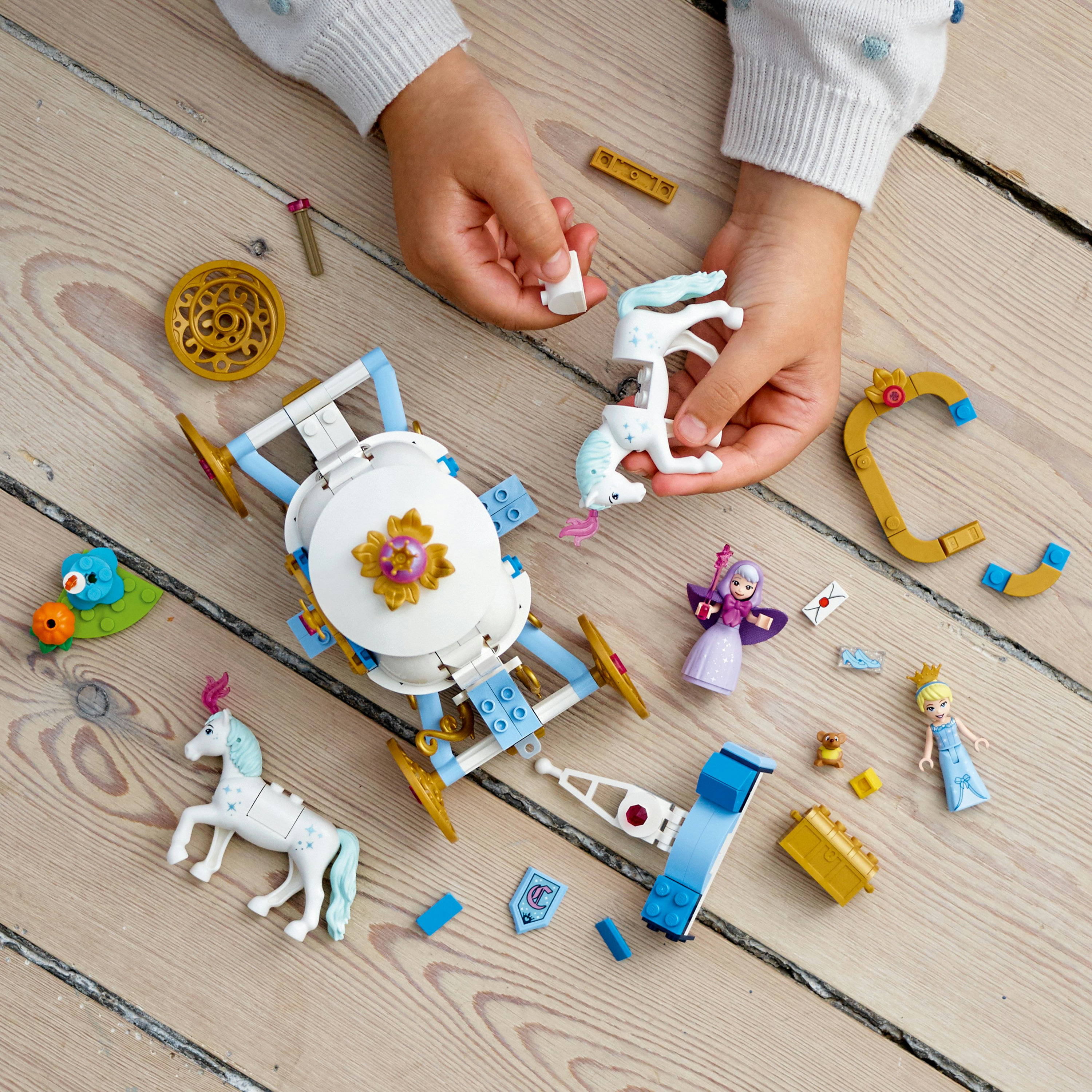Çocuğun elleri, tahta yüzeyde tek boynuzlu atlar, bir araba ve diğer temalı parçalarla bir Lego seti topluyor.