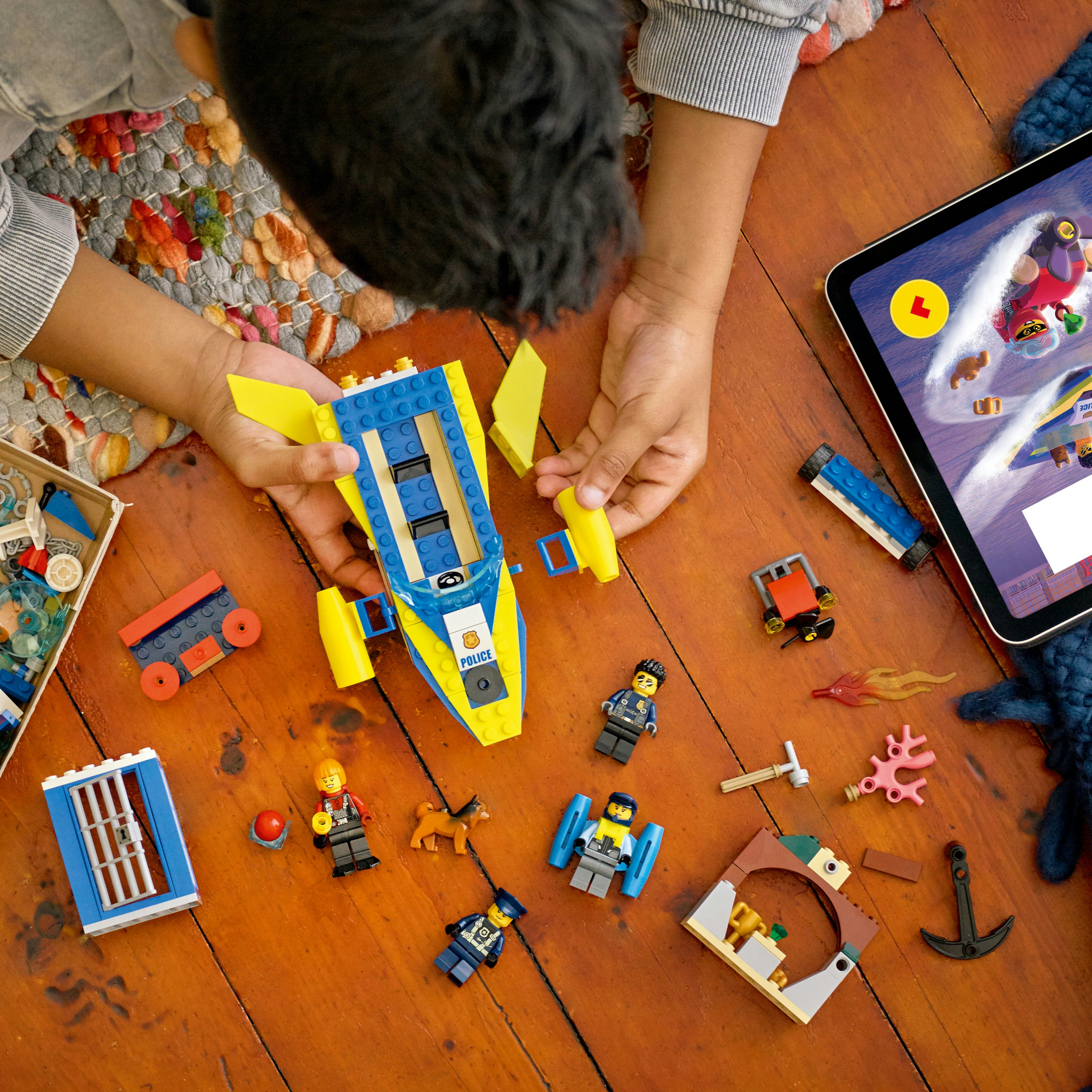 Enfant jouant avec un bateau de police Lego sur une surface en bois. Divers personnages et accessoires Lego.