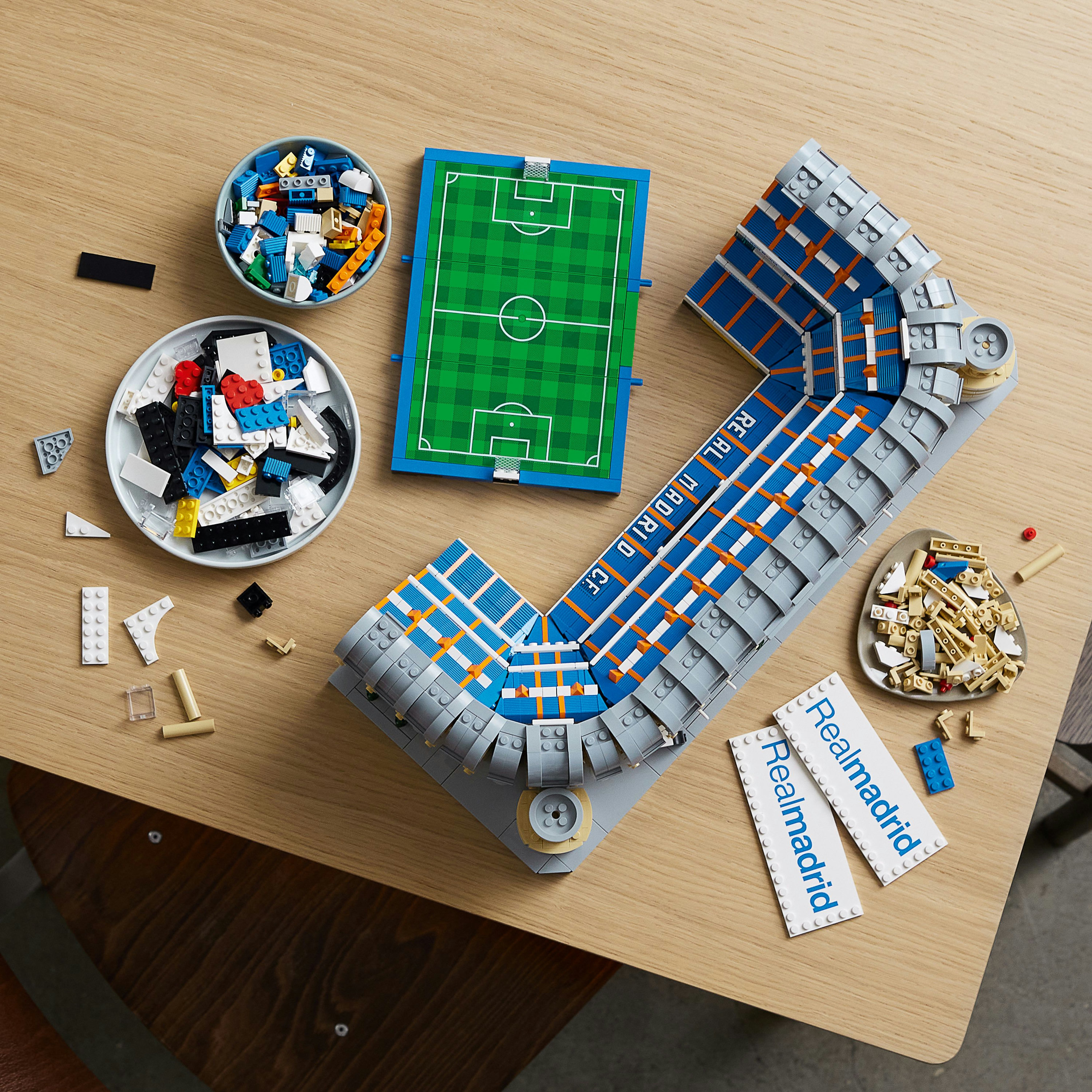 Lego Real Madrid stadyum parçaları, kaselerdeki parçalar ve bir futbol sahası.