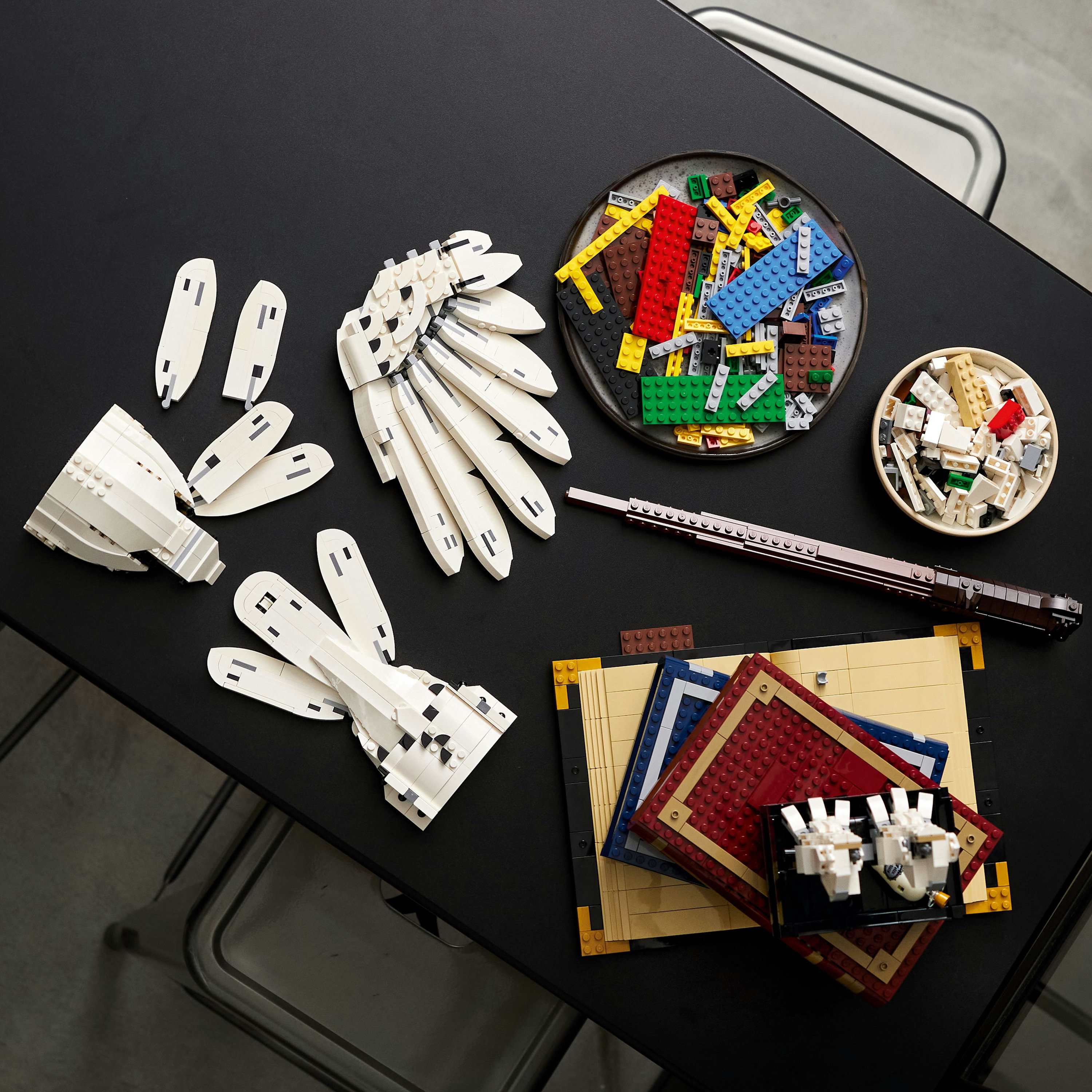 Elementy LEGO rozrzucone na czarnej powierzchni. Zawiera białe elementy i brązowy karabin.