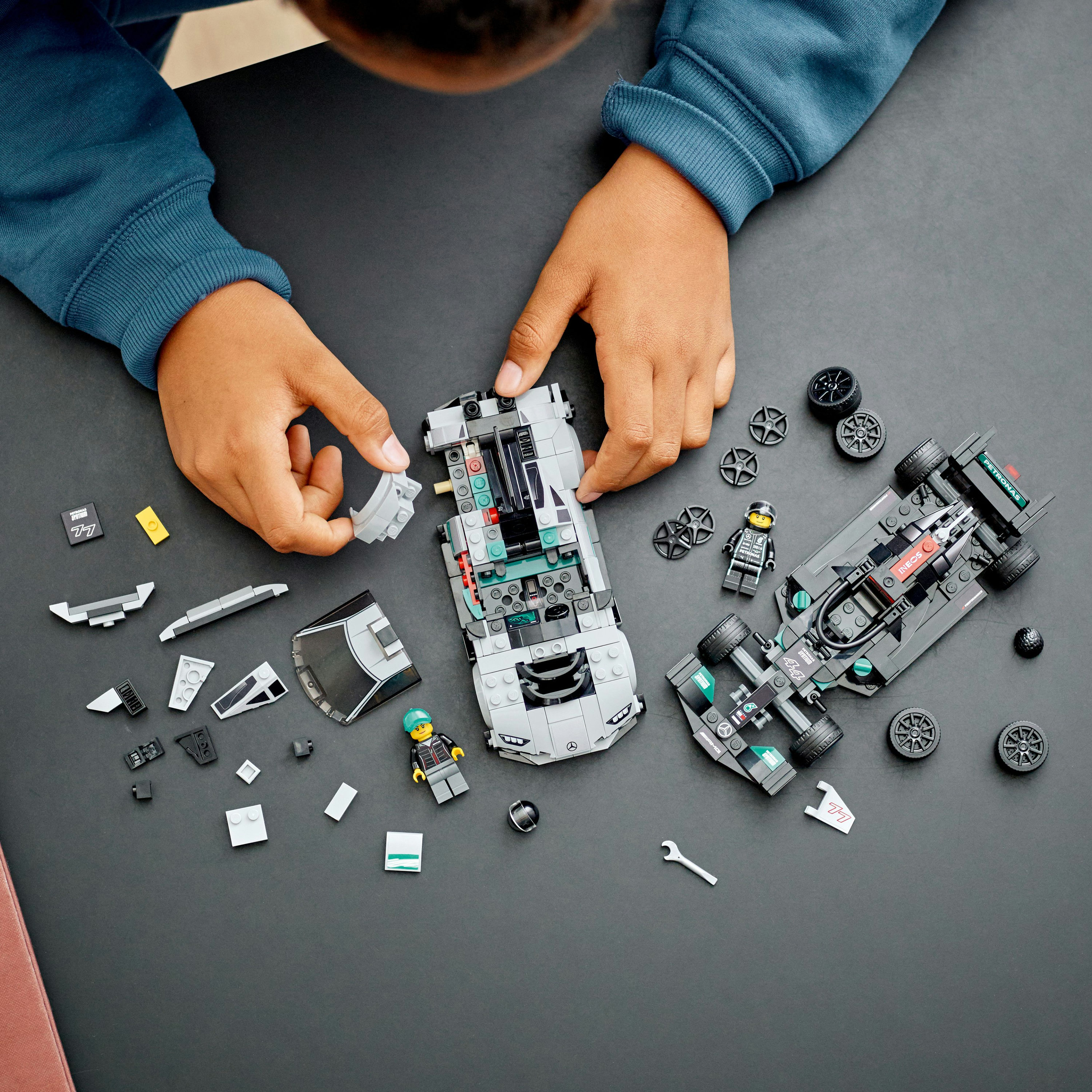 Un bambino che assembla un'auto da corsa Lego con varie parti. Lo sfondo è una superficie scura.