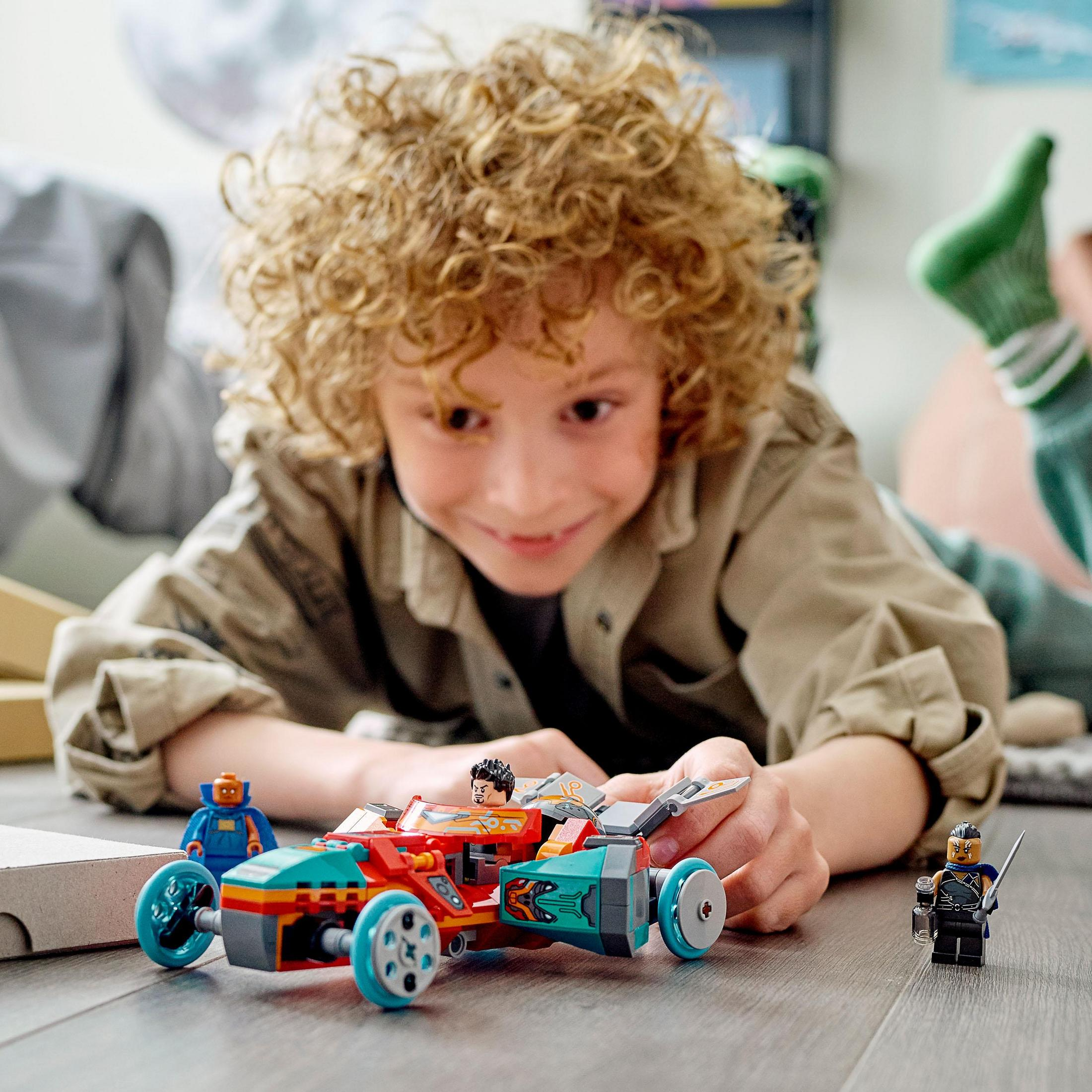 Ein Kind spielt mit einem LEGO Rennwagen-Set, mit Figuren und einem Rennwagen auf dem Boden.