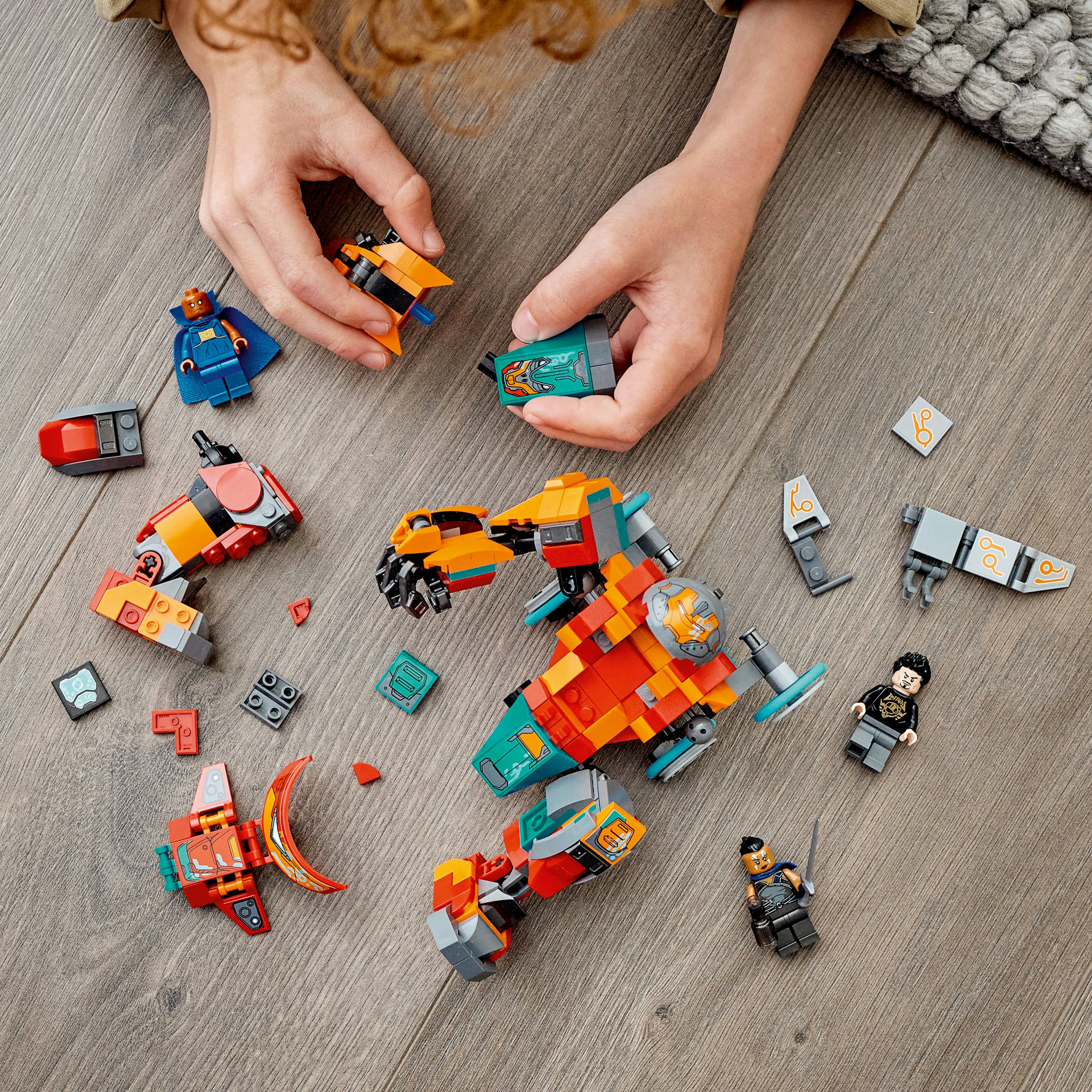 Ein Kind spielt mit Lego-Teilen. Verschiedene Lego-Figuren und Teile sind auf einem Holzboden verstreut.