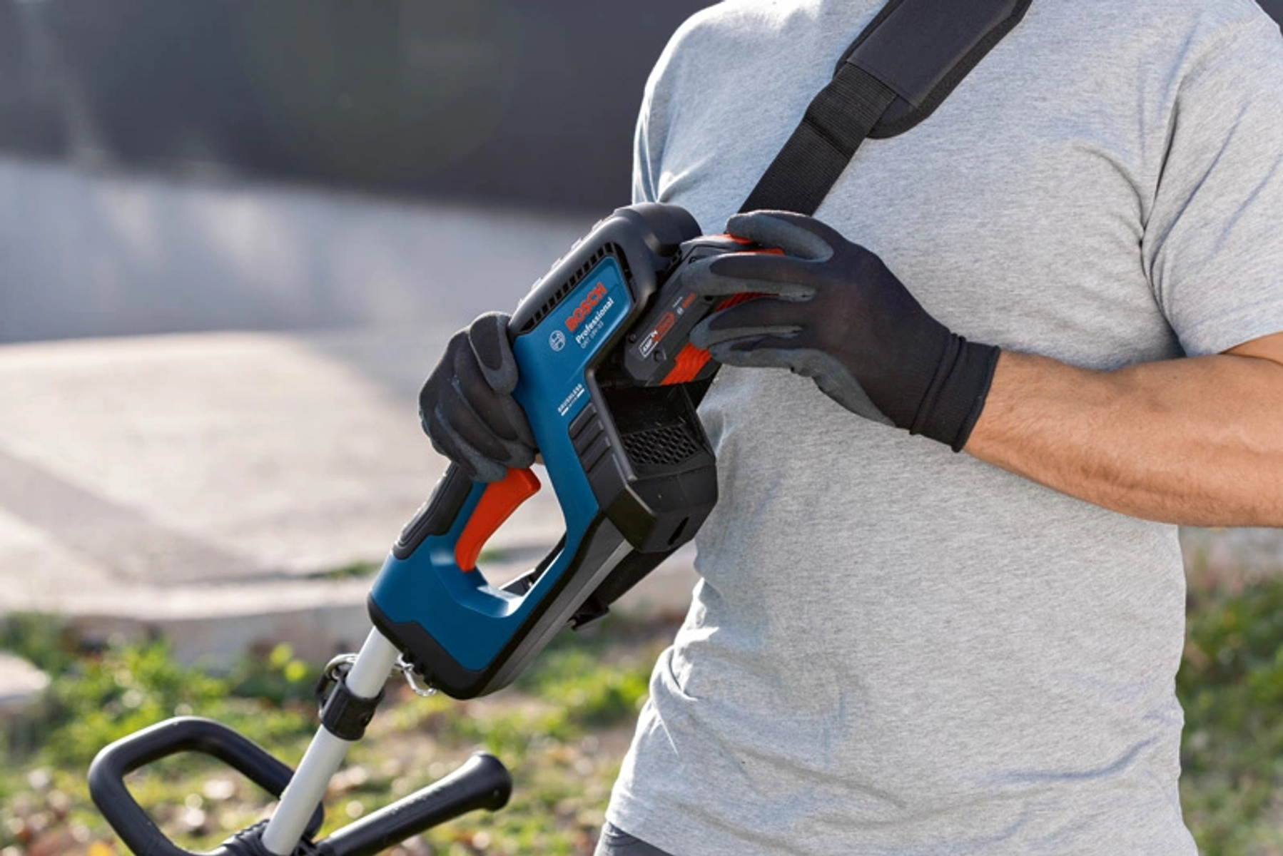 Una persona sostiene un cortador de césped inalámbrico Bosch profesional azul y negro con una correa negra.