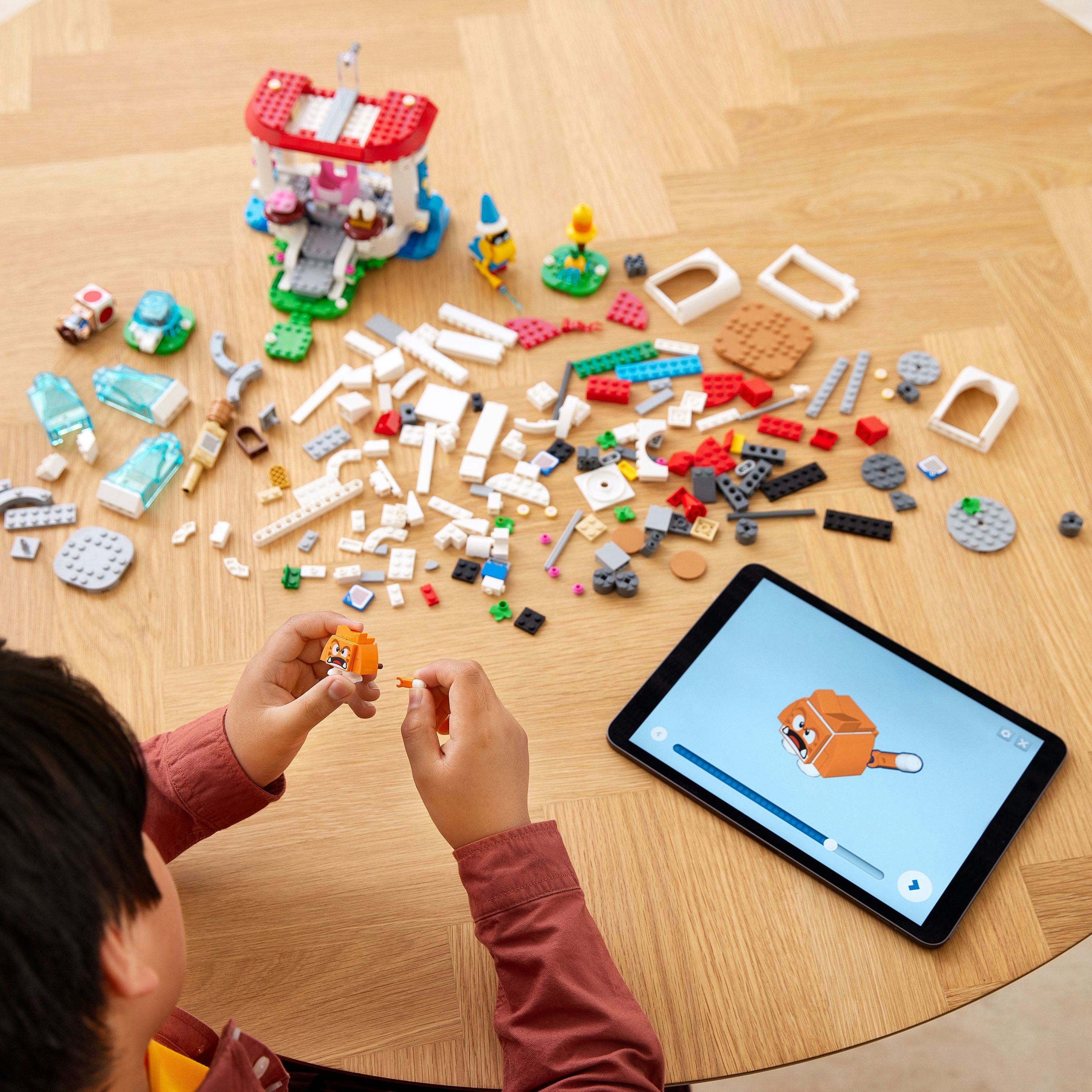 Un bambino costruisce un set LEGO su un tavolo, con un tablet che mostra le istruzioni e vari pezzi LEGO.