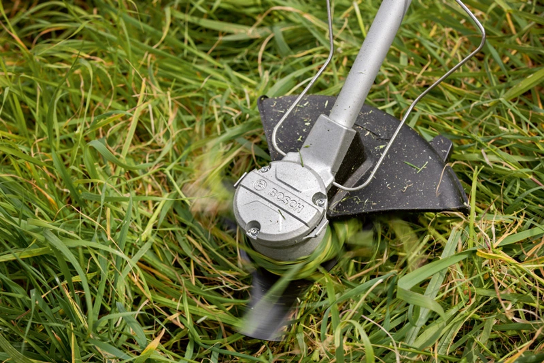 Nahaufnahme eines Rasentrimmers, der hohes Gras schneidet. Der Trimmer ist silber und schwarz.