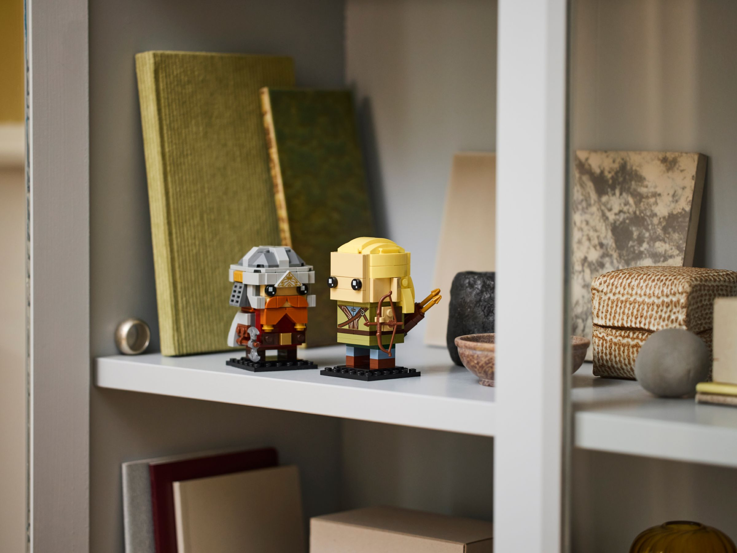 Due personaggi Lego su una mensola con libri e altri oggetti. Mensola e sfondo bianchi.