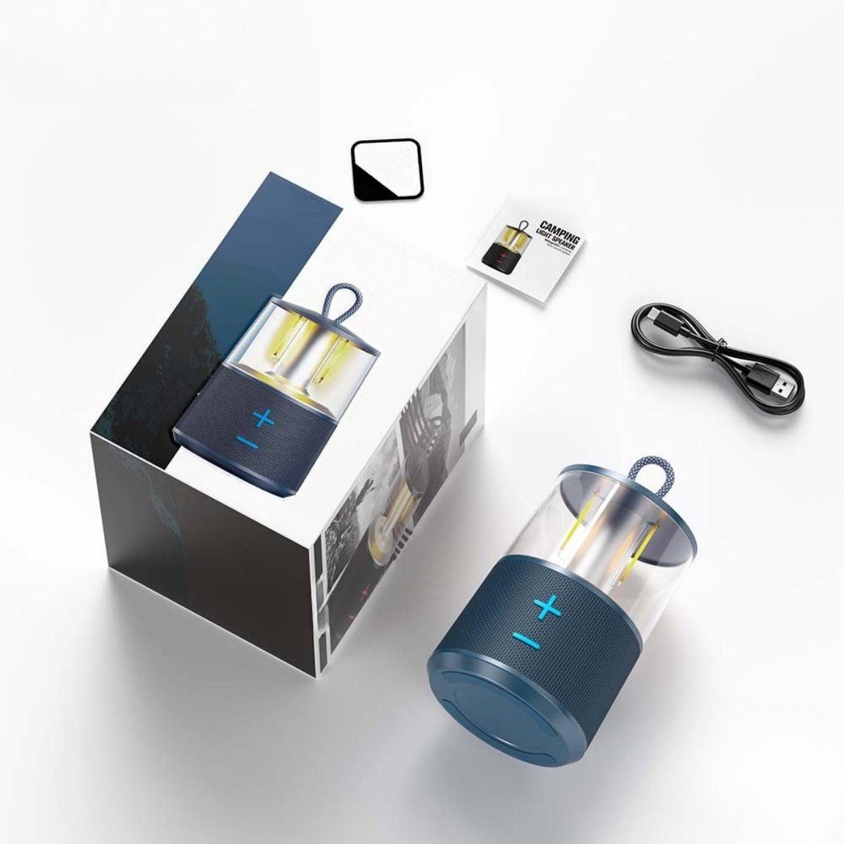 Ein Lautsprecher und seine Verpackung. Der Lautsprecher ist blau und hat ein Pluszeichen. Ein USB-Kabel ist sichtbar.