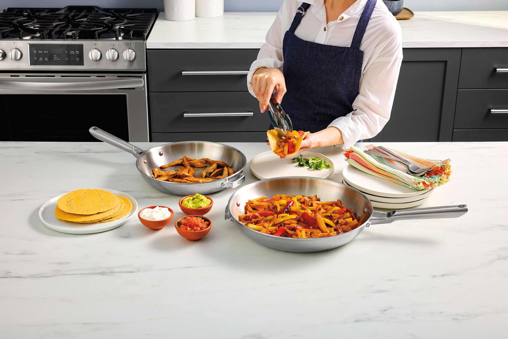 Osoba przygotowująca jedzenie na patelniach, z tortillami, salsą i guacamole. Ustawienia kuchni ze sprzętem ze stali.