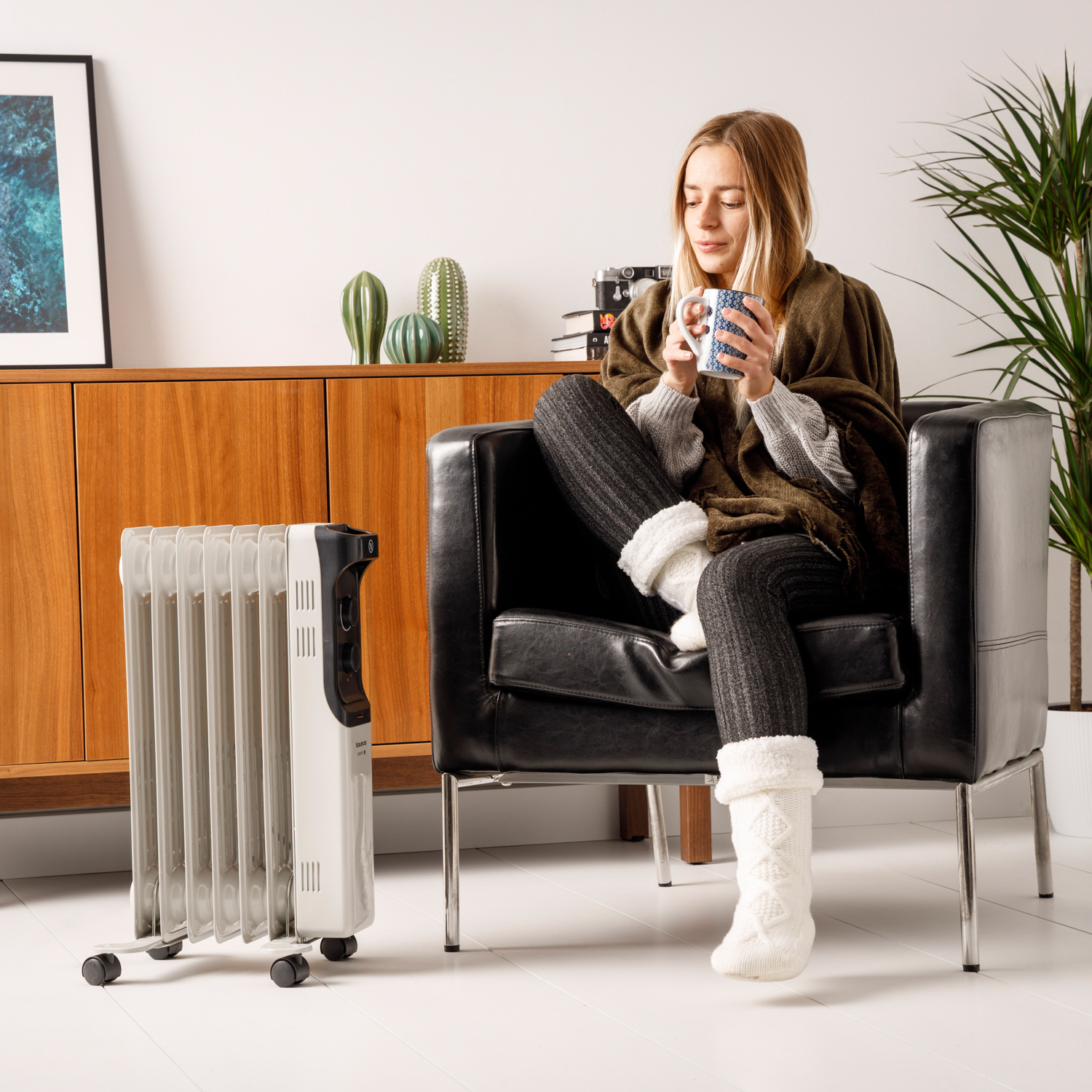 Kobieta pije z kubka, siedząc w czarnym fotelu z kaloryferem obok, przytulna sceneria.