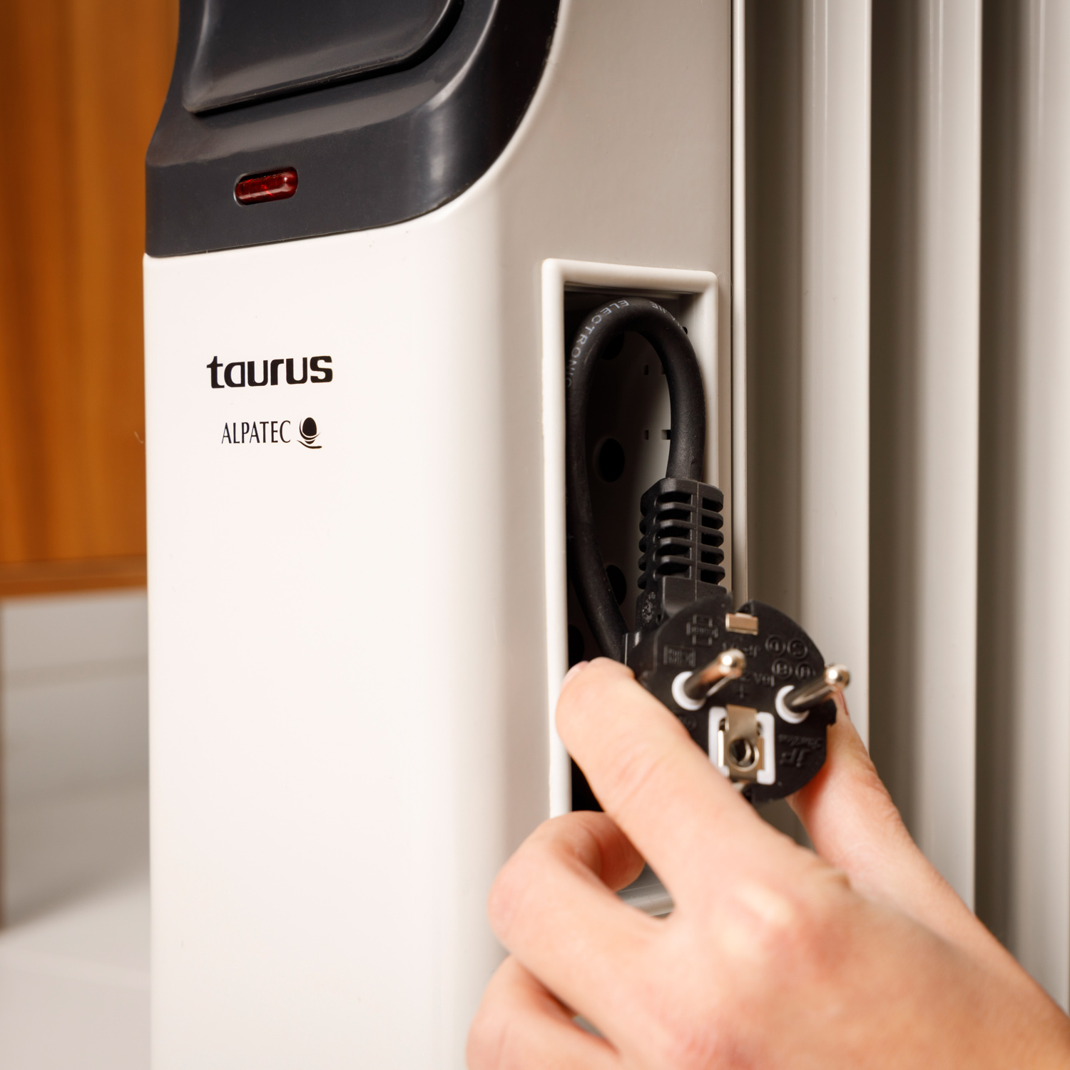 Osoba podłączająca przewód zasilający do białego grzejnika z marką „Taurus”.