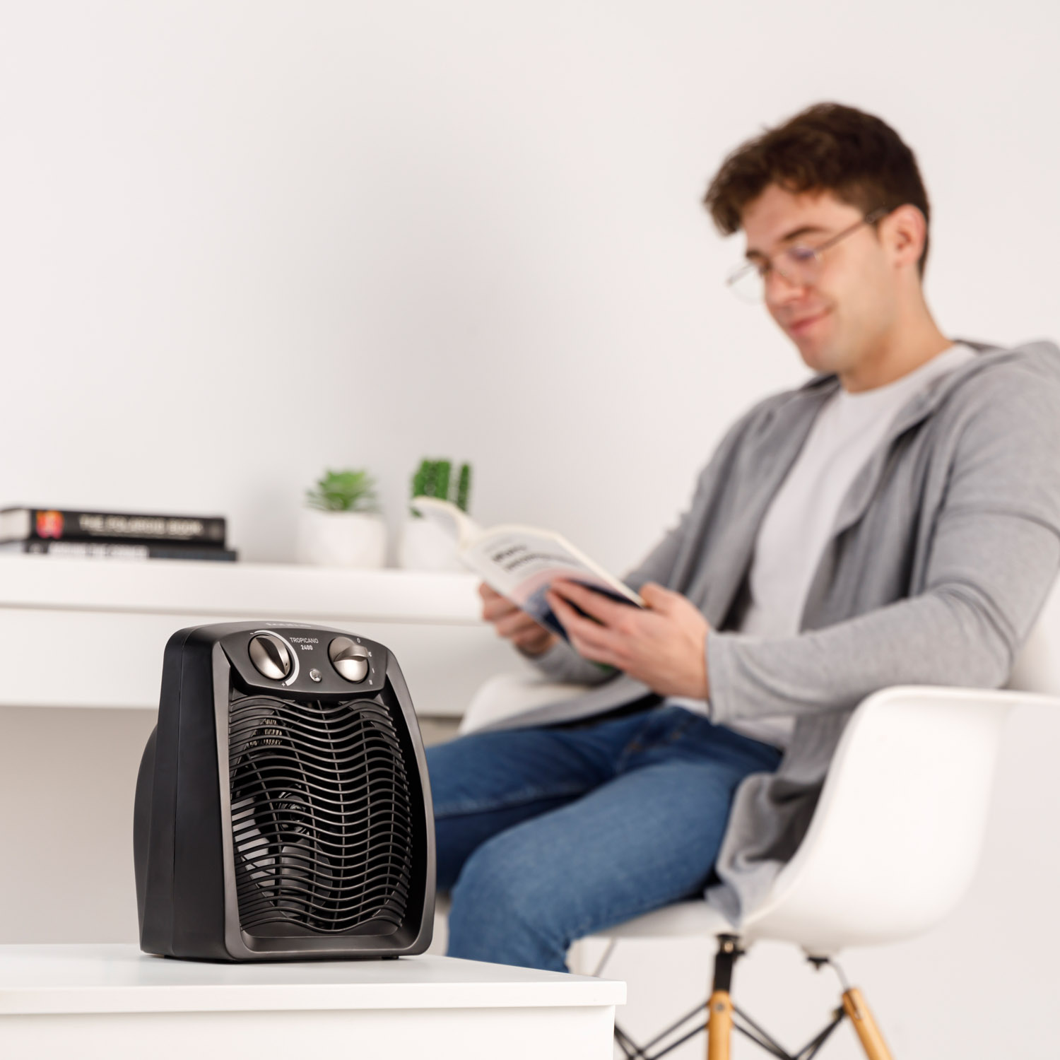 Czarny grzejnik na białym stole z mężczyzną czytającym książkę w tle.