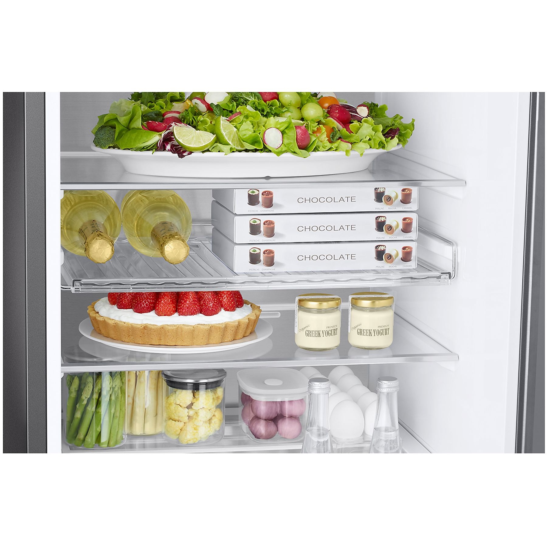 Interno del frigorifero: insalata, cioccolatini, torta, yogurt e bottiglie sugli scaffali.