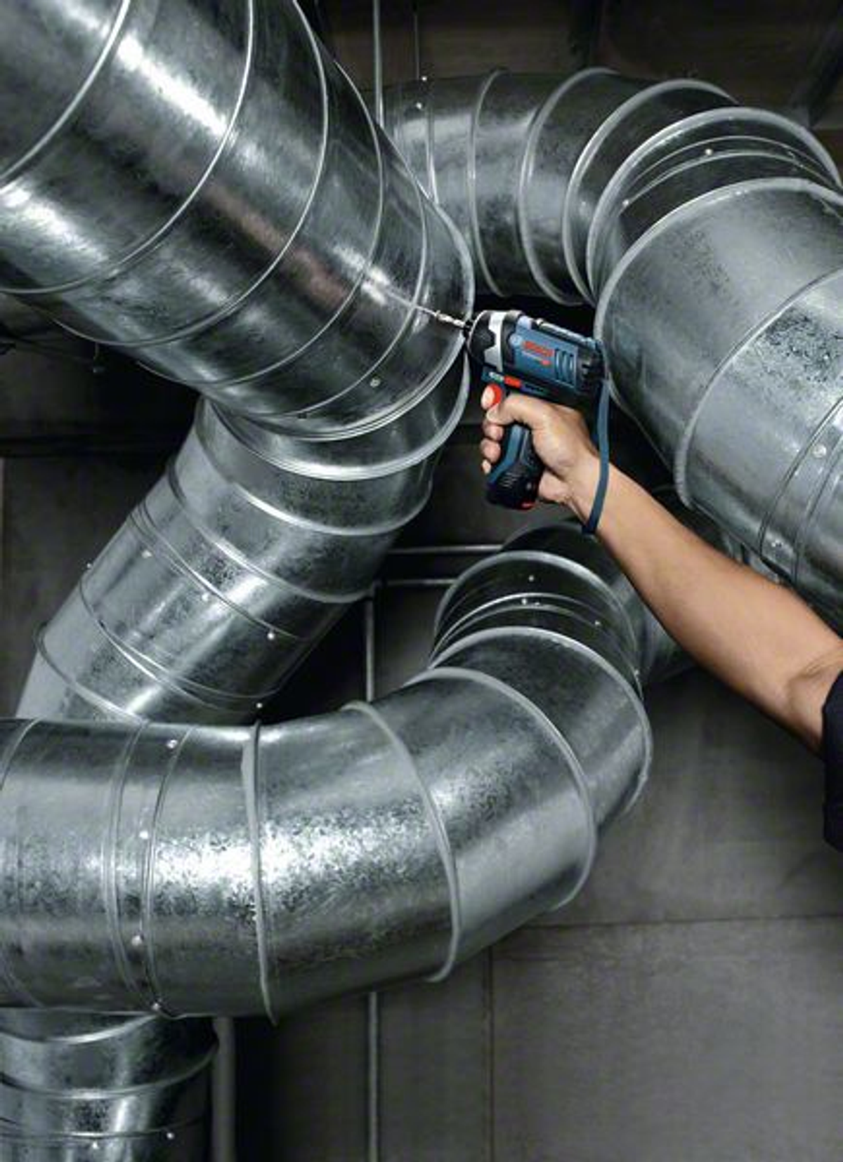 Osoba używająca niebiesko-czarnej wiertarki na srebrnym metalowym kanale.