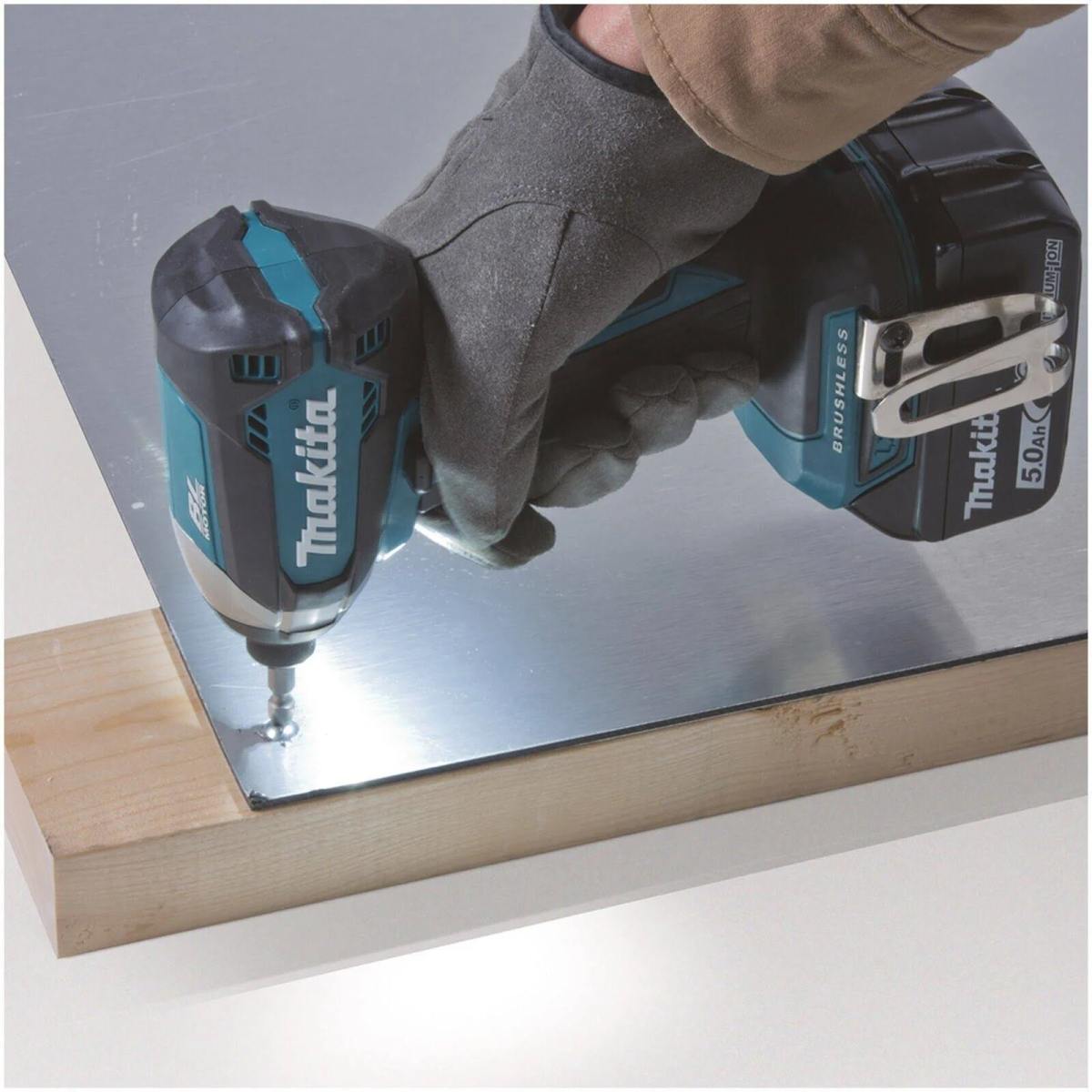 Zakrętarka udarowa Makita wkręca śrubę w blachę nad drewnianym klockiem.