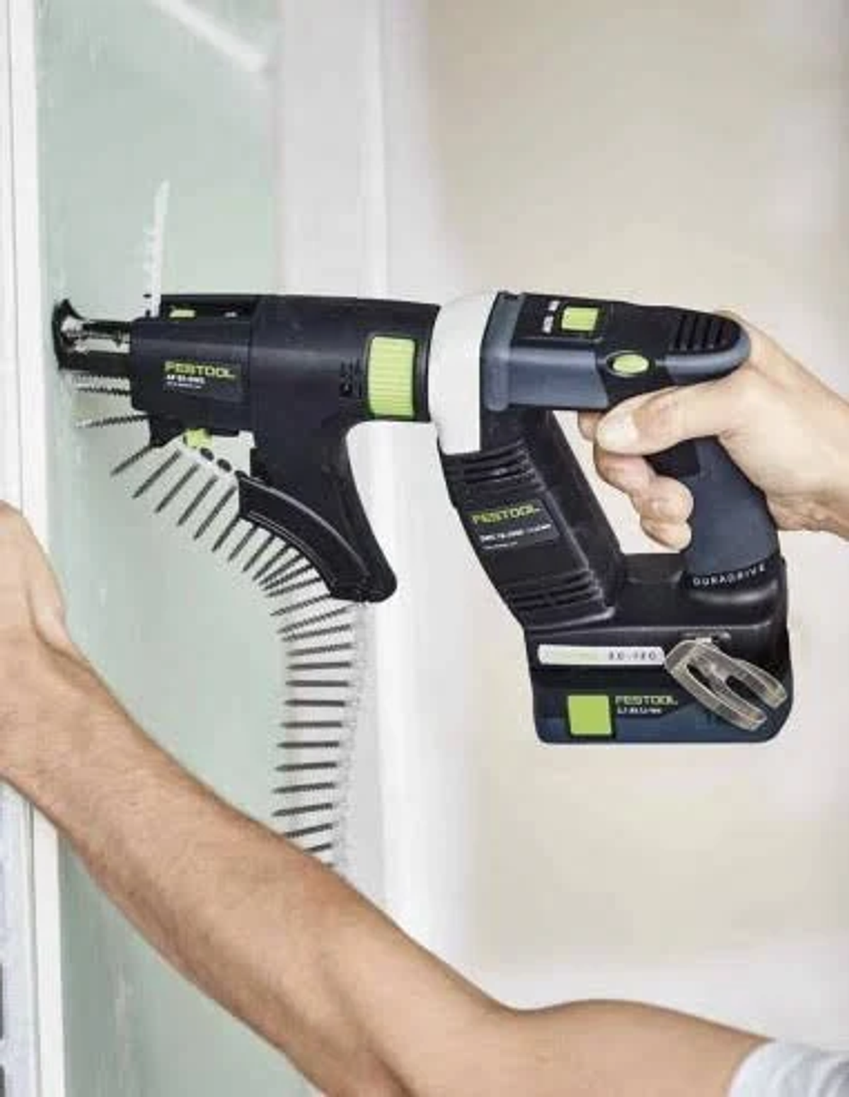 Osoba używa czarno-zielonej wkrętarki akumulatorowej do przymocowania płyty gipsowo-kartonowej do ściany.