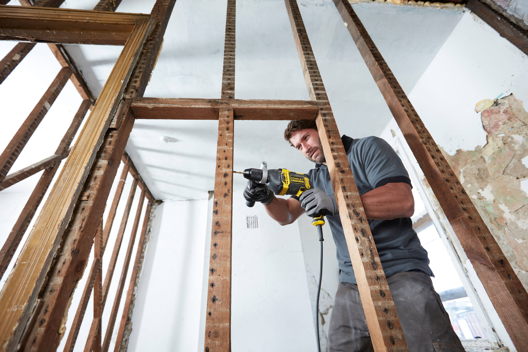 Un hombre taladrando un marco de madera con un taladro eléctrico, en un entorno de construcción interior.