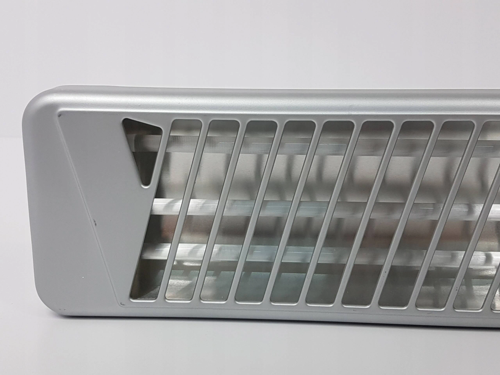 Srebrny grzejnik elektryczny z pionowymi otworami wentylacyjnymi, widoczny z bliska.