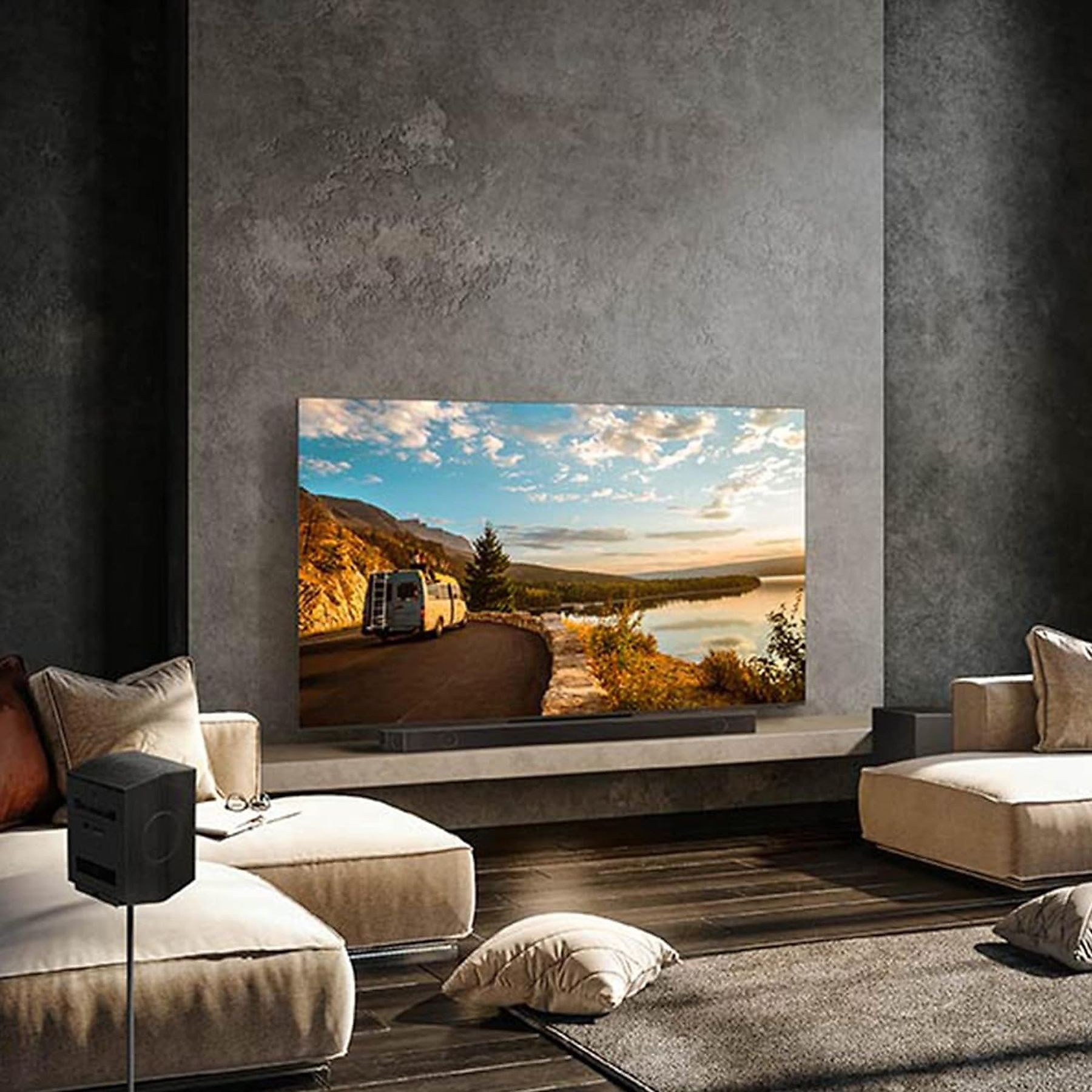Wohnzimmer mit großem Fernseher, Soundbar und Lautsprechern. Eine Straßenszene wird auf dem Bildschirm angezeigt.