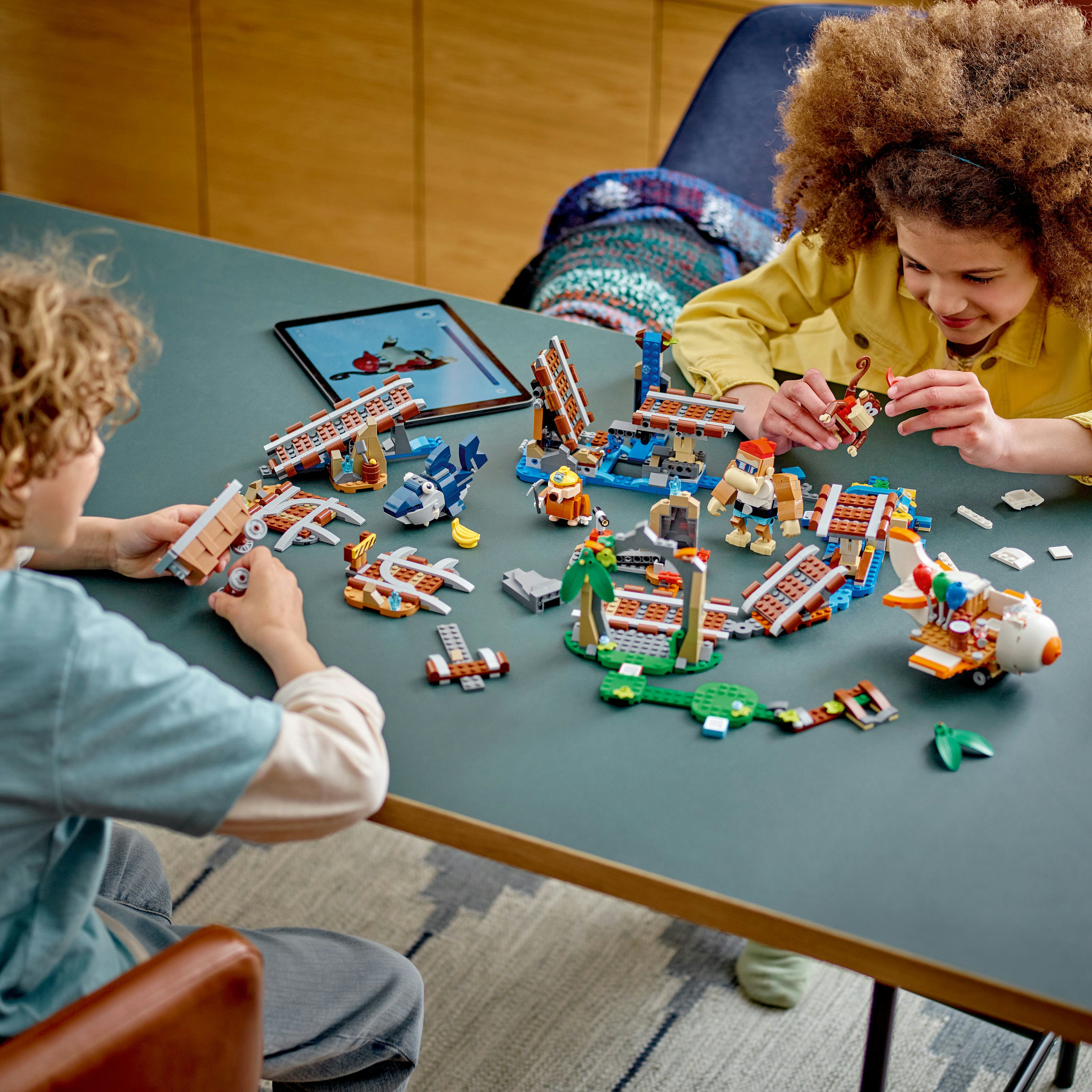 Twee kinderen bouwen Lego sets op een tafel met een tablet.